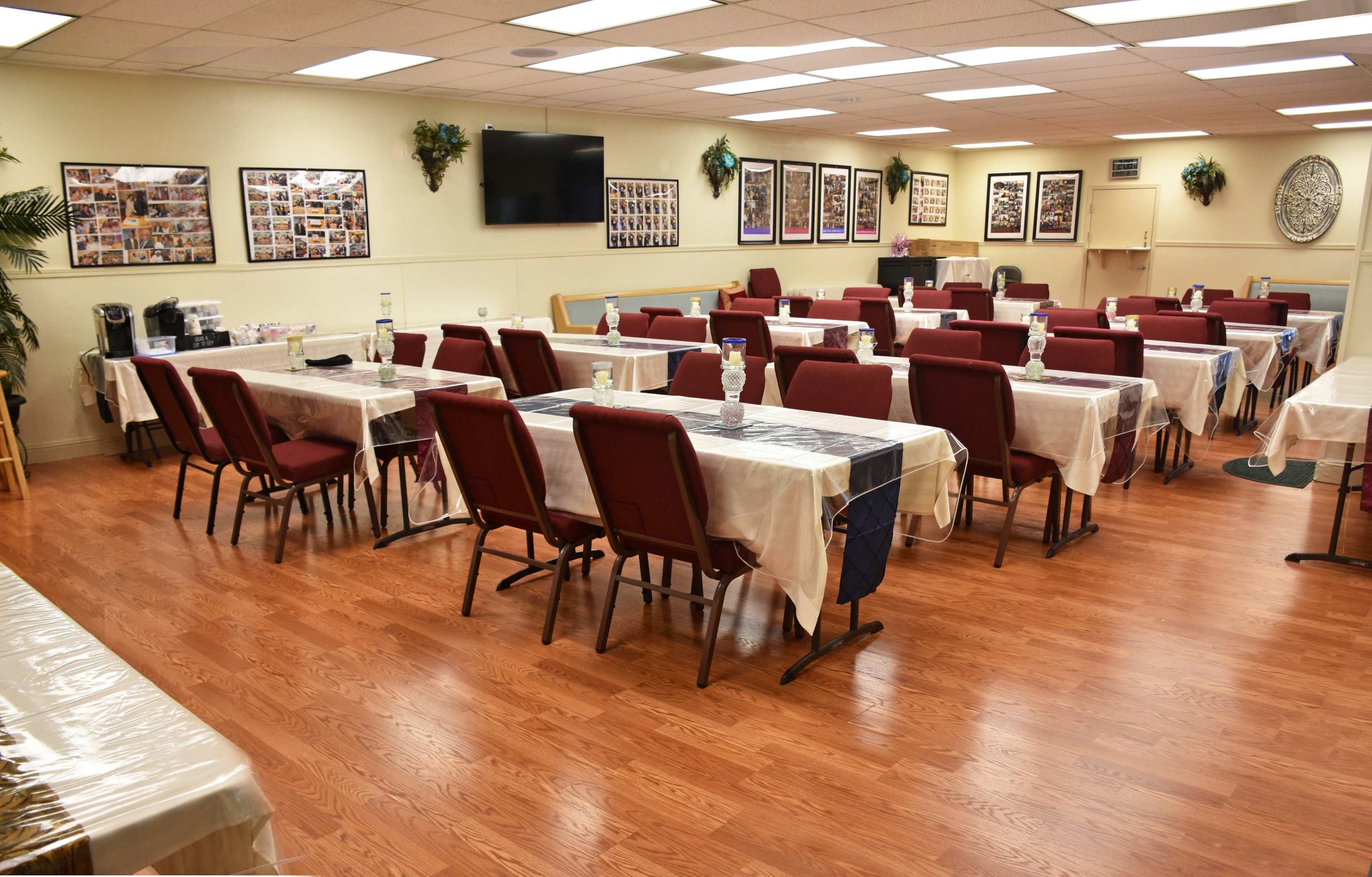 A spacious dining area with several tables covered in white tablecloths and arranged with chairs facing each table, surrounded by walls adorned with framed photographs.