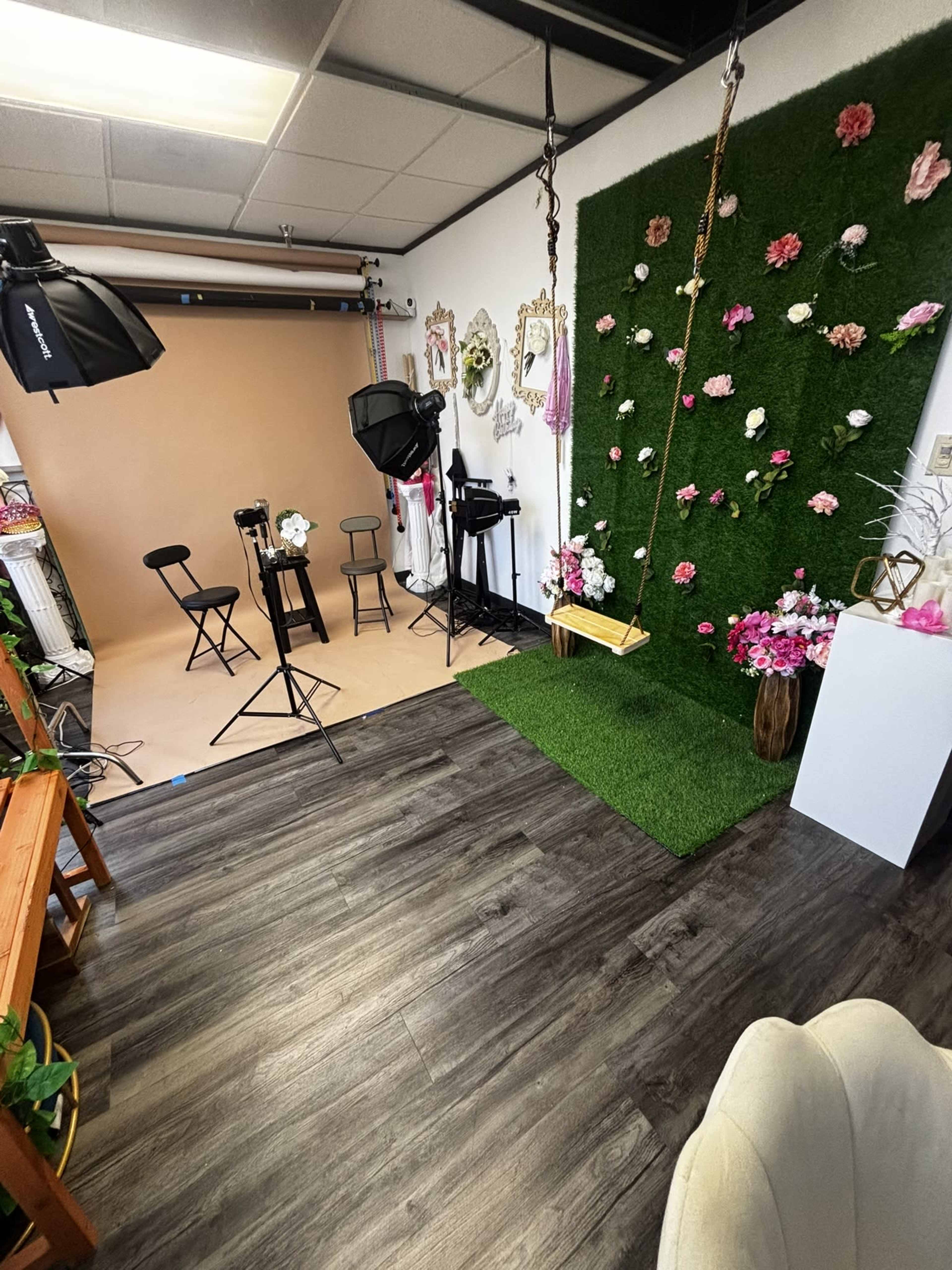 The image shows a photography studio setup featuring a swing, floral decorations, backdrop, and lighting equipment arranged in a well-decorated space.