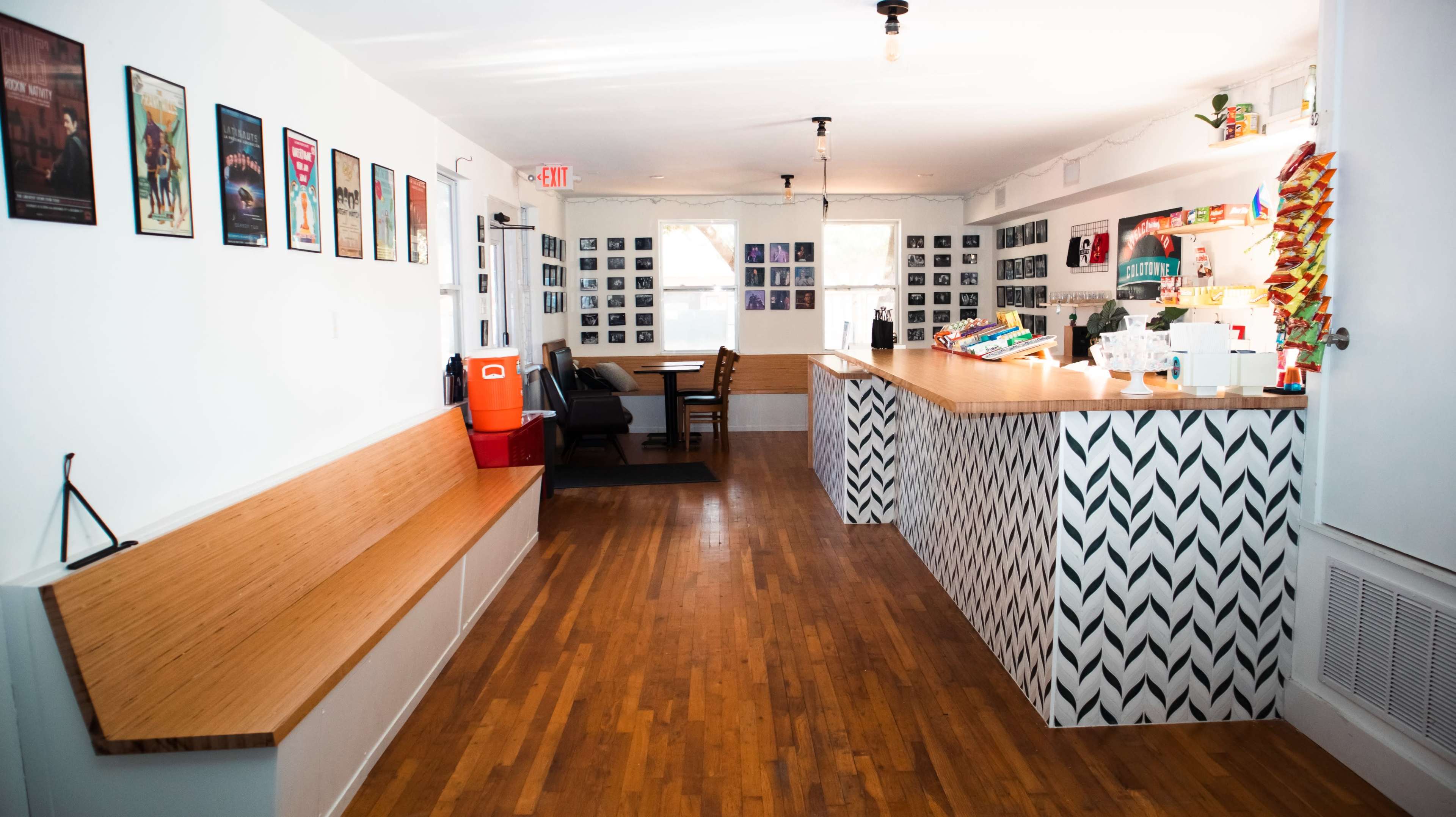 The image shows a brightly lit café interior featuring wooden floors, a patterned counter, and walls adorned with various framed photos.