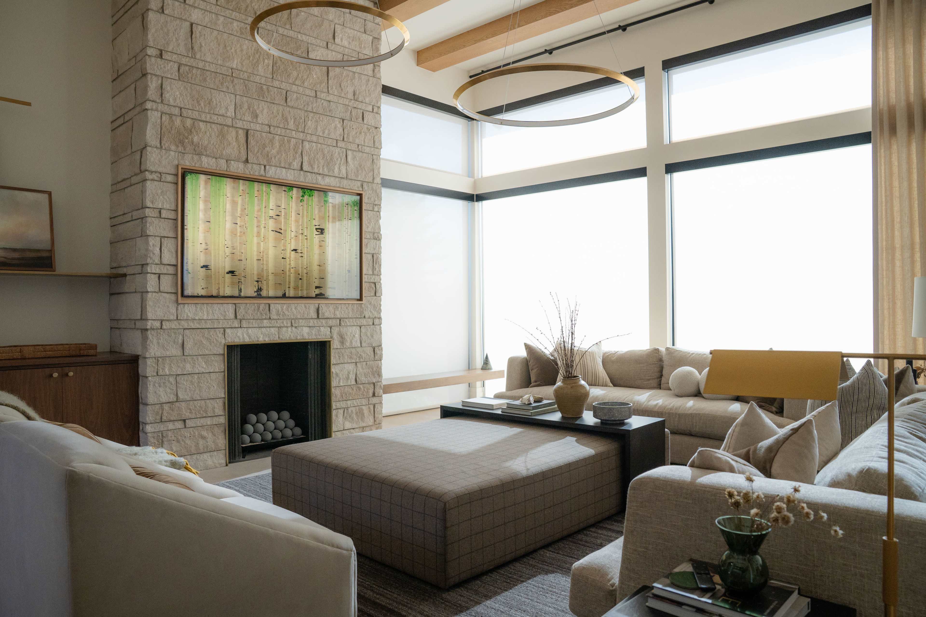 The image shows a modern living room with a stone fireplace, large windows, and a central coffee table surrounded by sofas.
