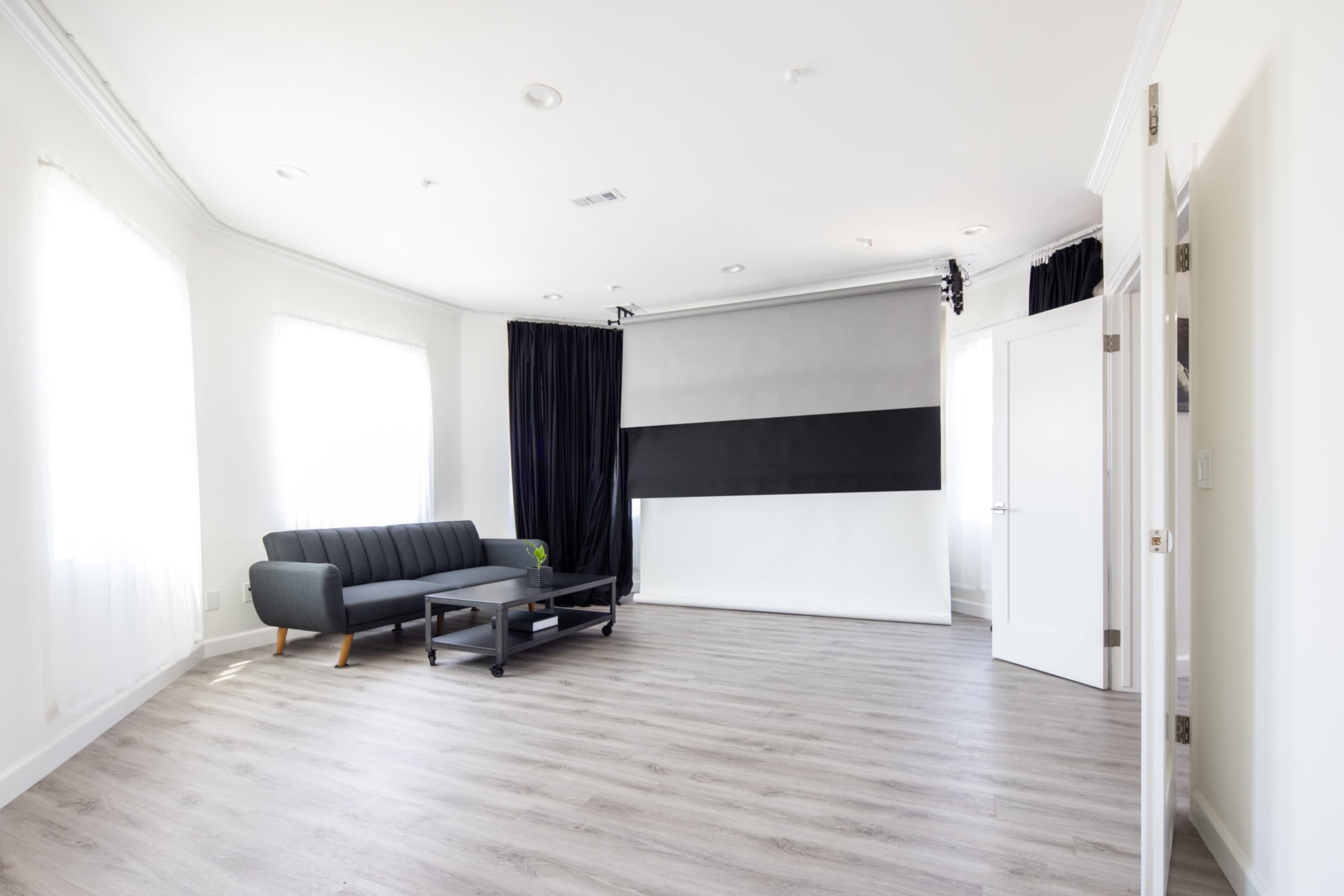 A spacious, well-lit room featuring a gray sofa, a coffee table, and a large window with sheer curtains.