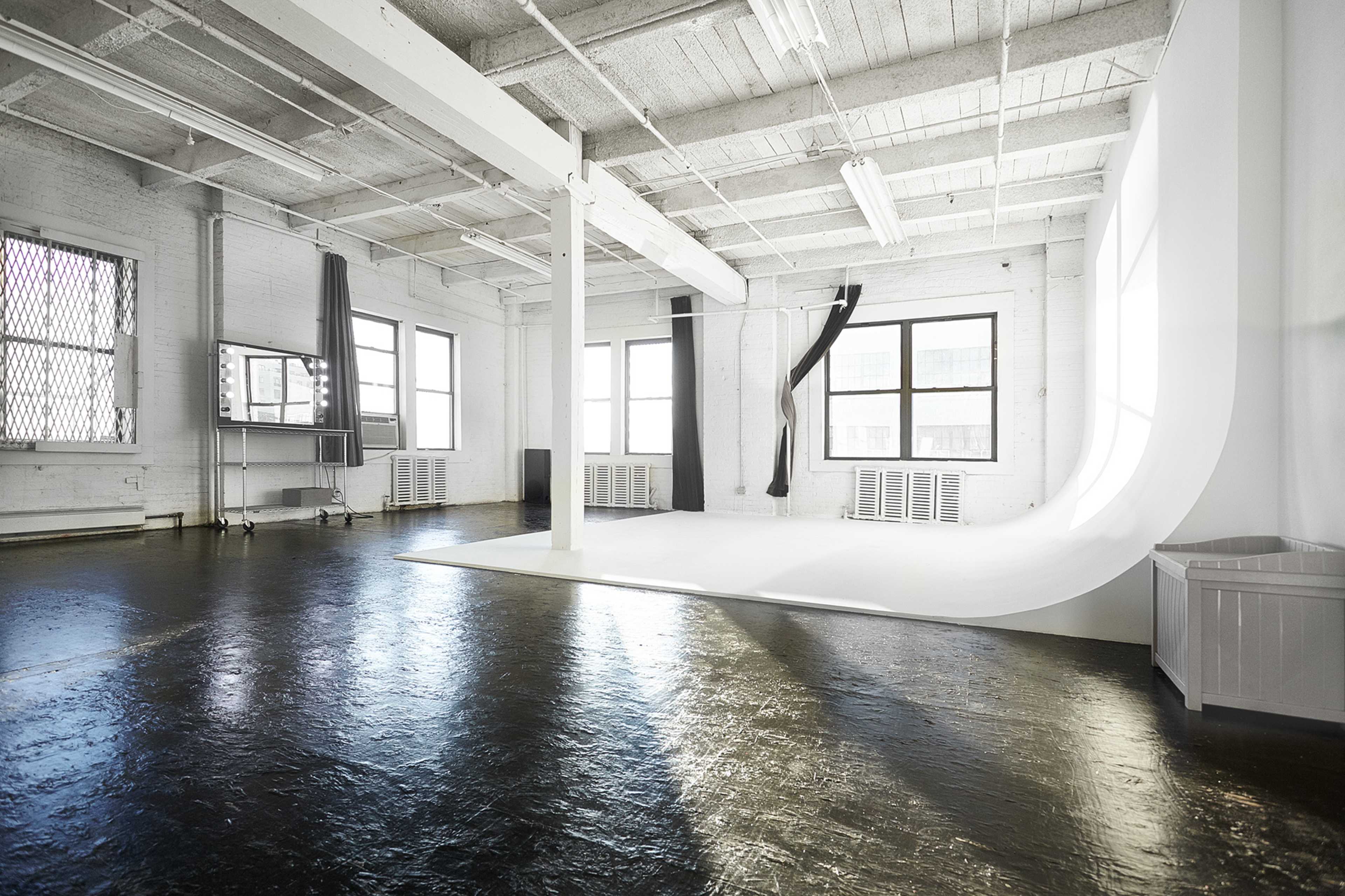 A spacious, well-lit studio with large windows, a curved white backdrop, and polished dark floors.