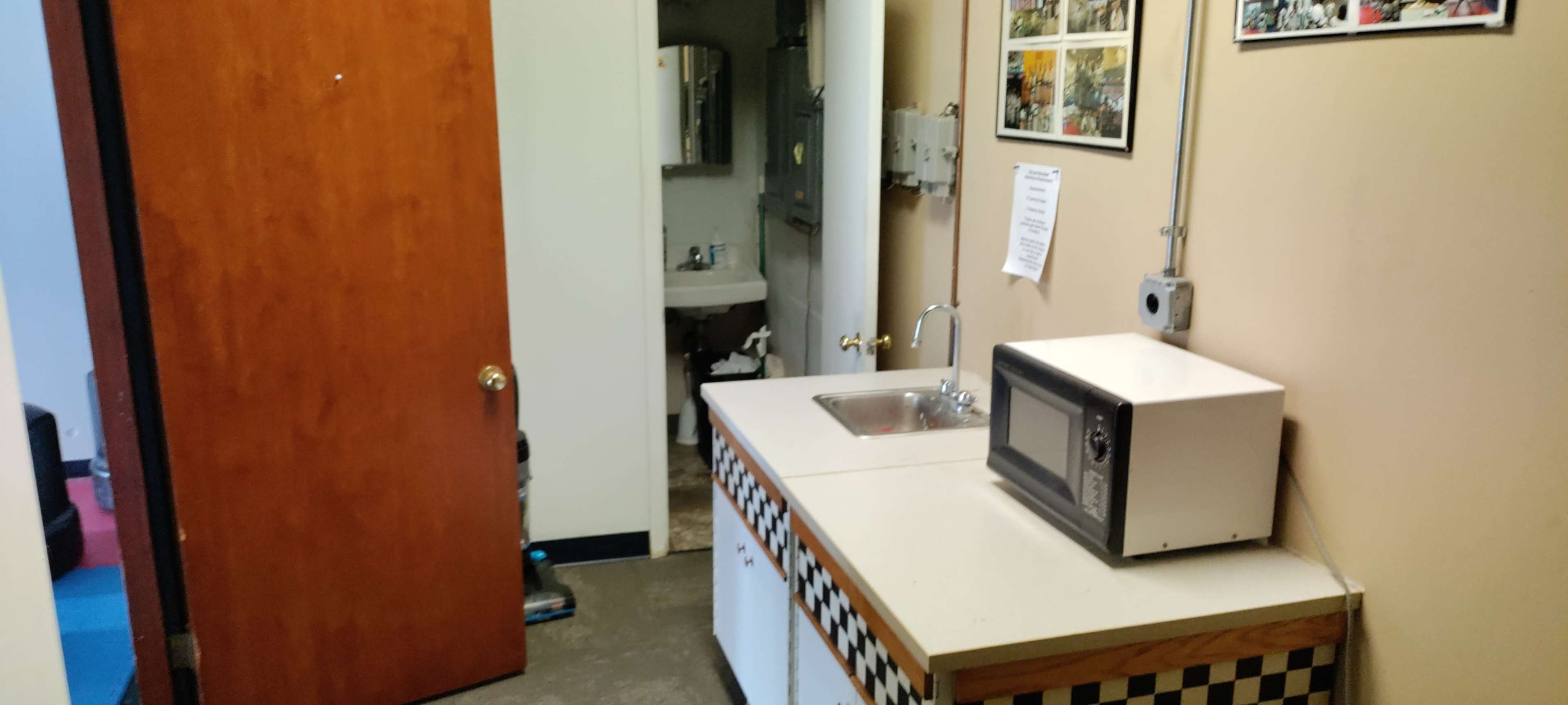 A small kitchenette with a microwave, sink, and a door leading to a restroom area.