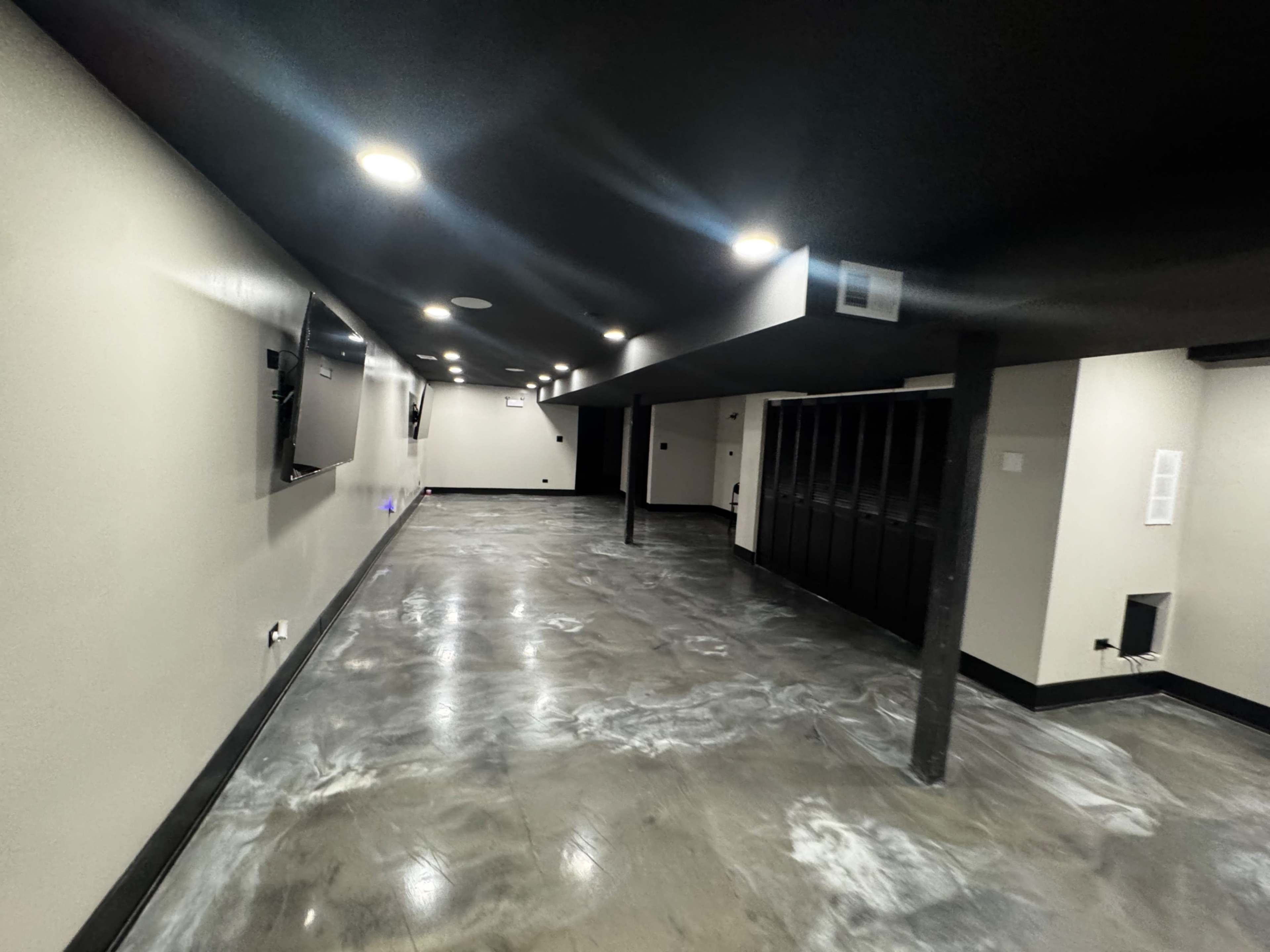 The image shows a spacious, unfinished basement with a polished concrete floor and minimal lighting along the ceiling.