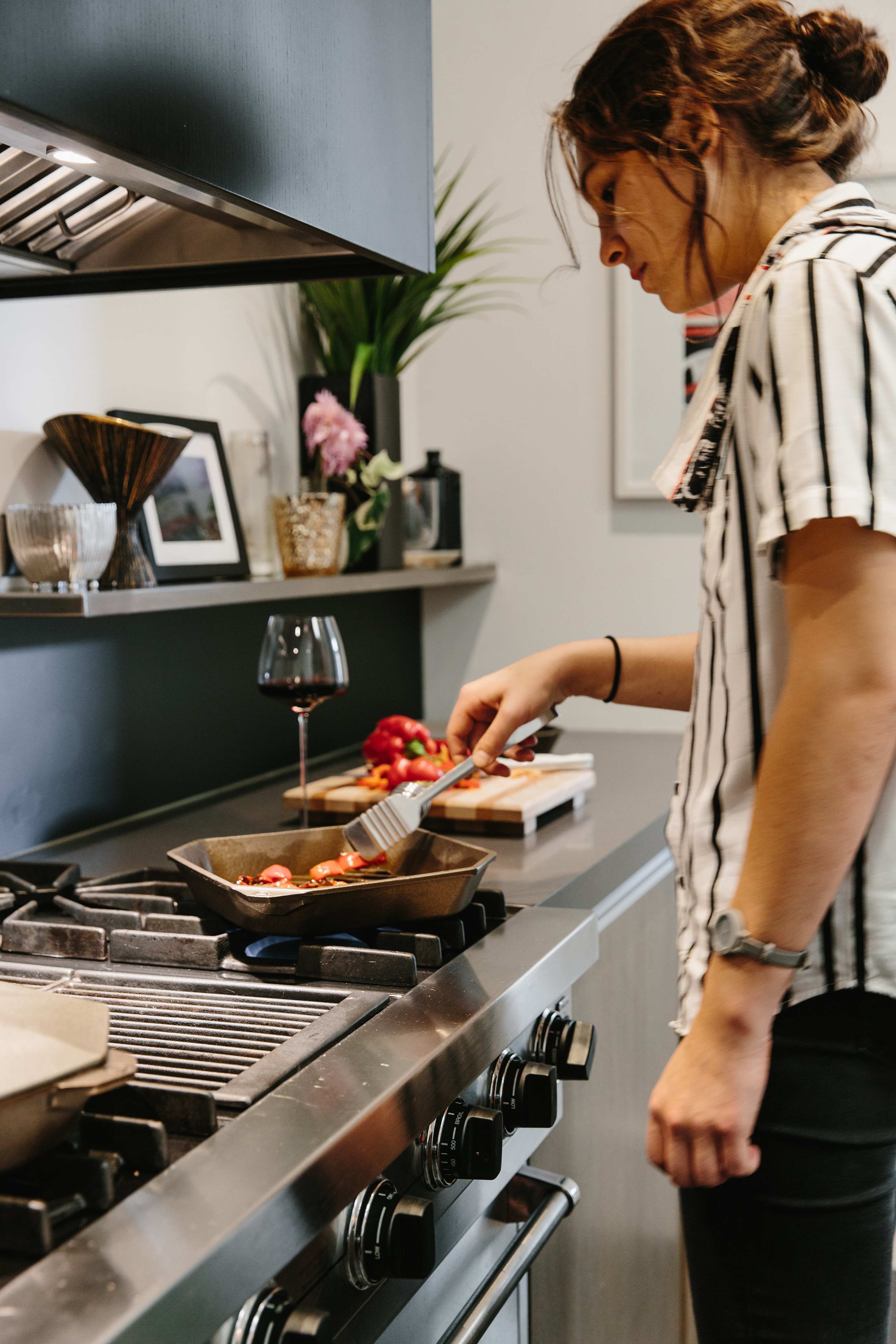 A woman is cooking on a stovetop in a modern kitchen while stirring ingredients in a skillet.