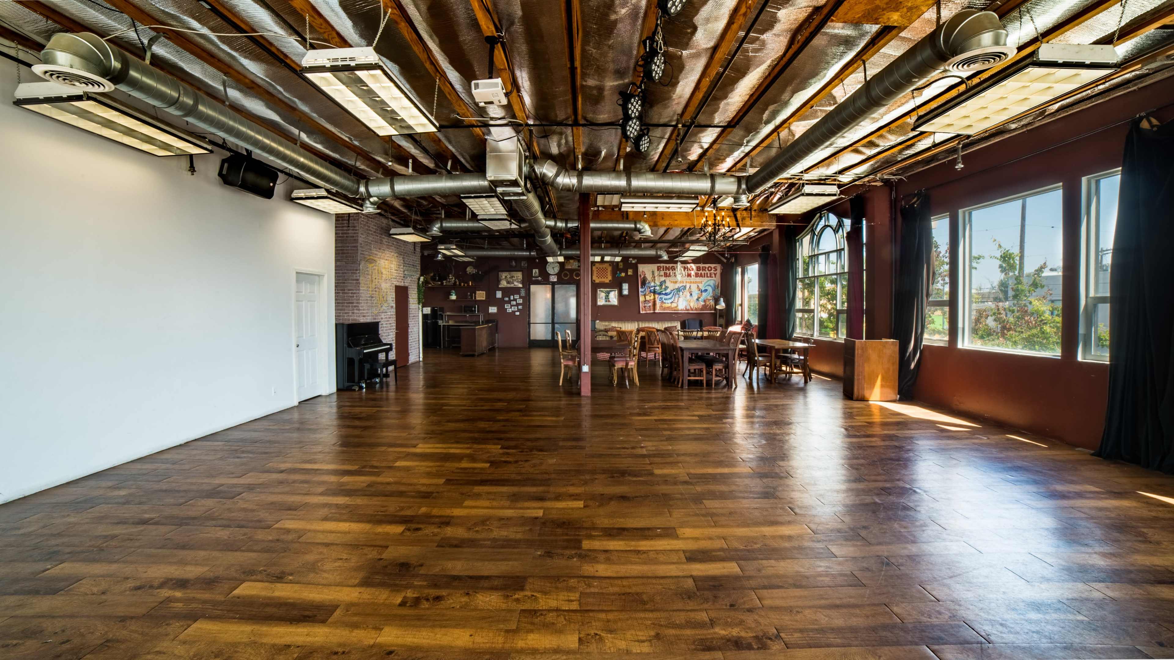 A spacious interior room with hardwood flooring, exposed beams, and large windows allowing natural light.