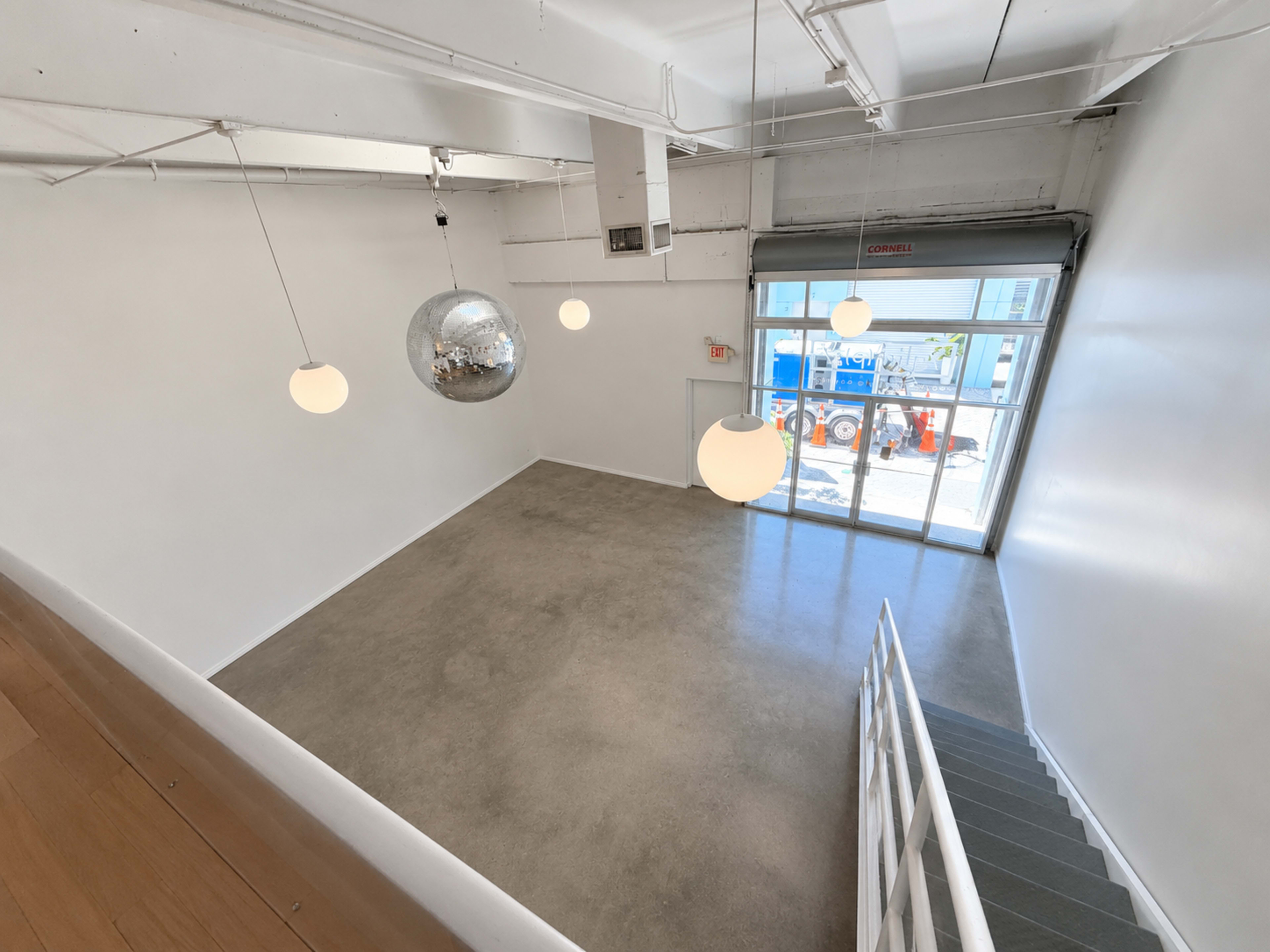 The image shows a spacious, empty room with polished concrete floors, large windows, and modern light fixtures, including a disco ball.