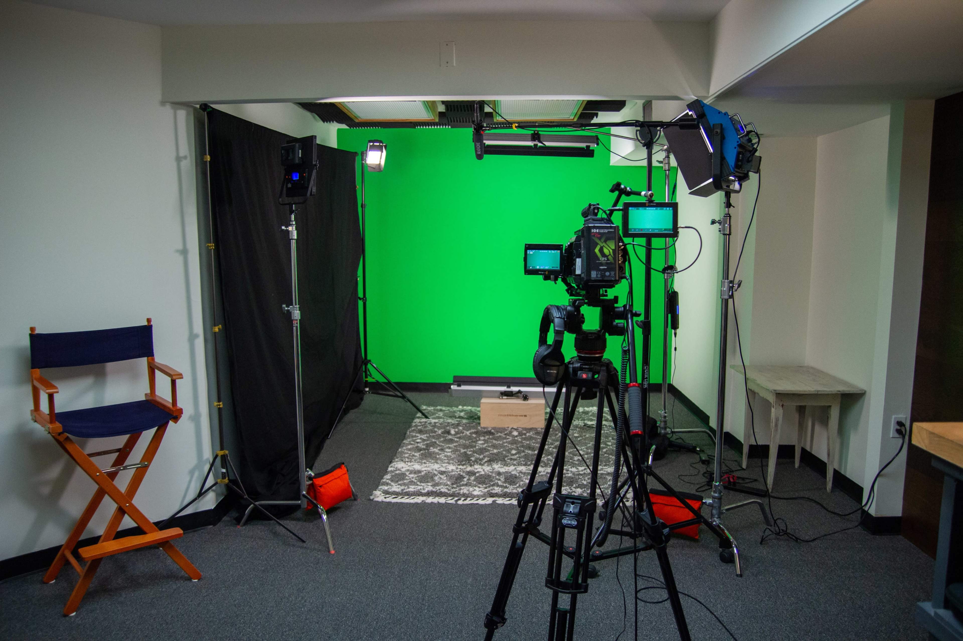 A recording studio setup with a green screen, lighting equipment, and a director's chair.