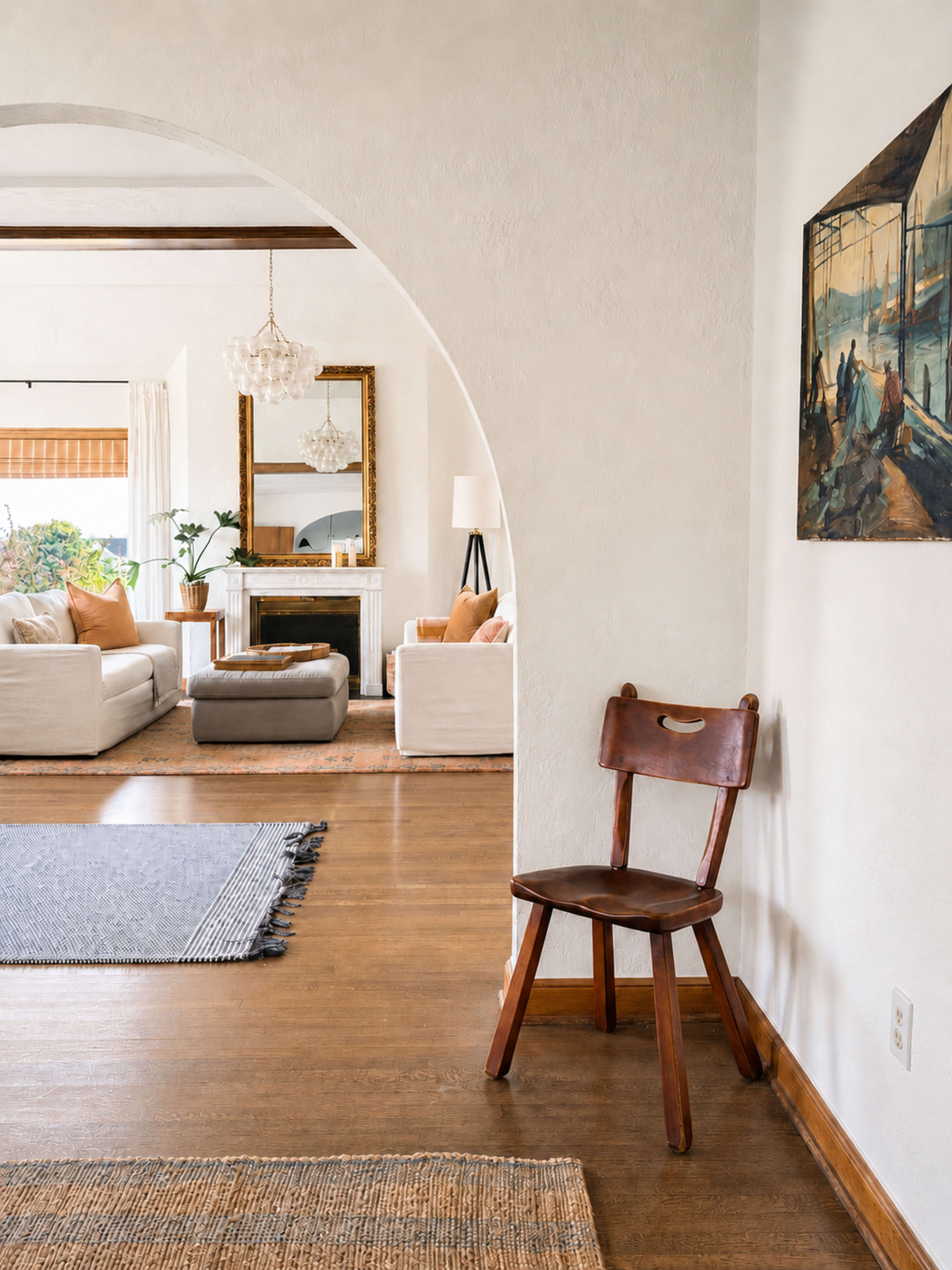 A wooden chair stands against a wall in a well-lit living space, featuring a cozy seating area with a modern design and a decorative painting.