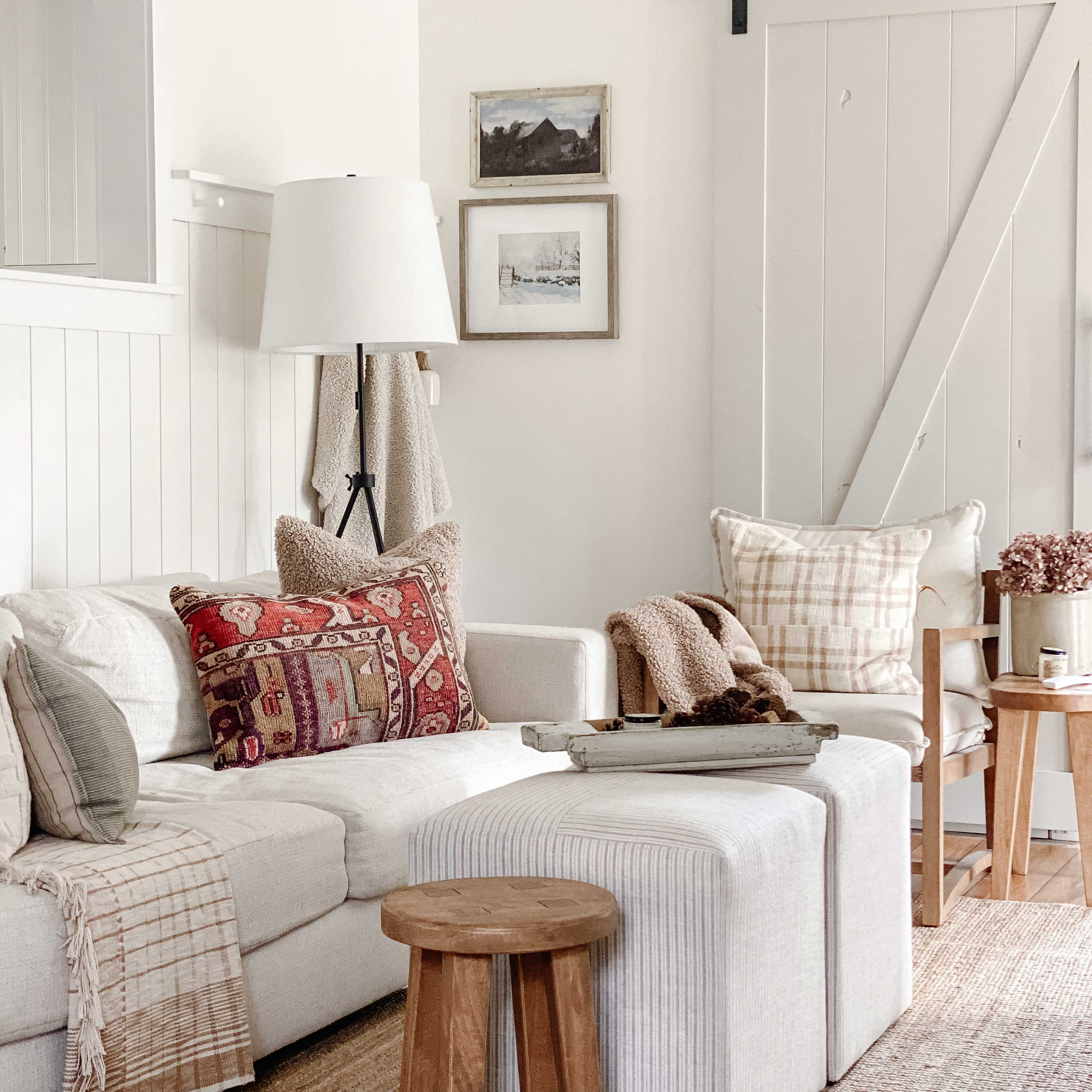 The image shows a cozy living room with a light-colored sofa adorned with decorative pillows, a wooden coffee table in the center, and framed art on the walls.