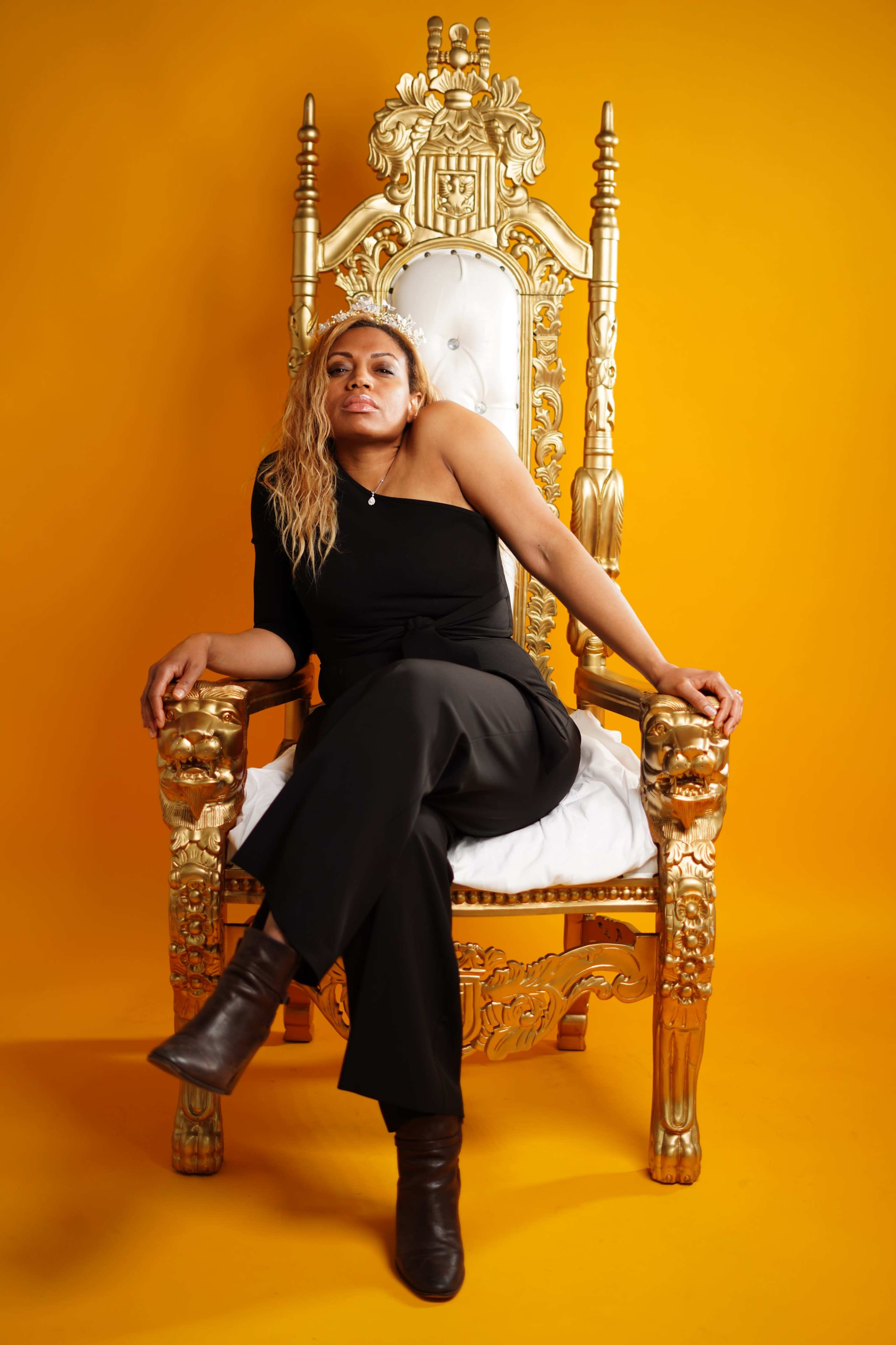 A person sits on an ornate golden throne against a bright yellow background.