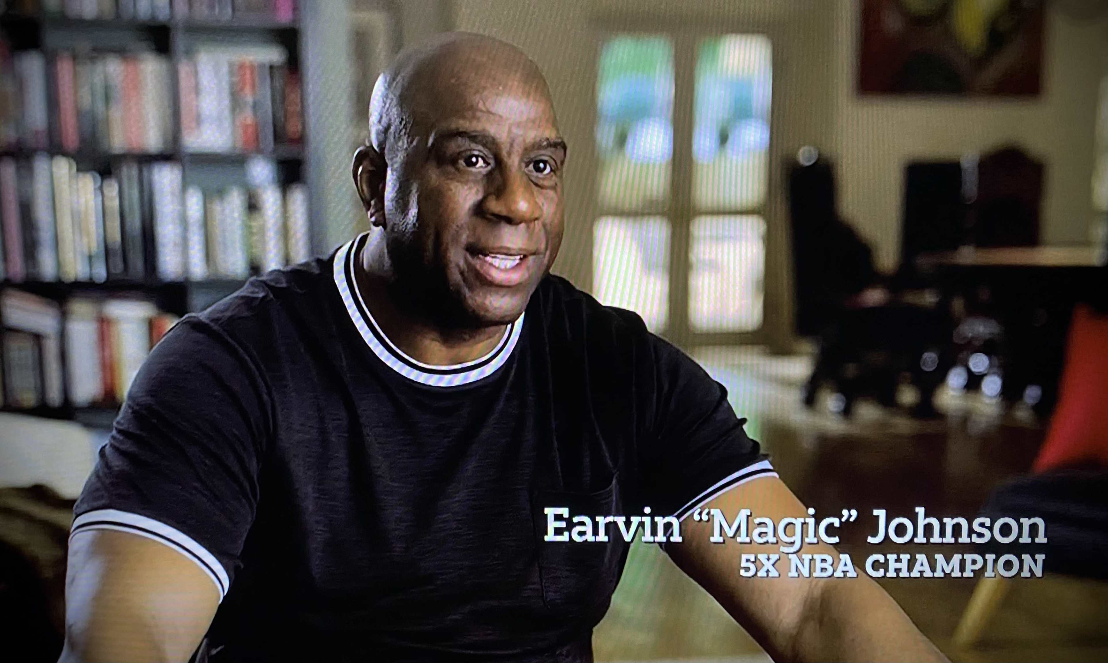 A man sitting indoors is identified as Earvin "Magic" Johnson, a five-time NBA champion.