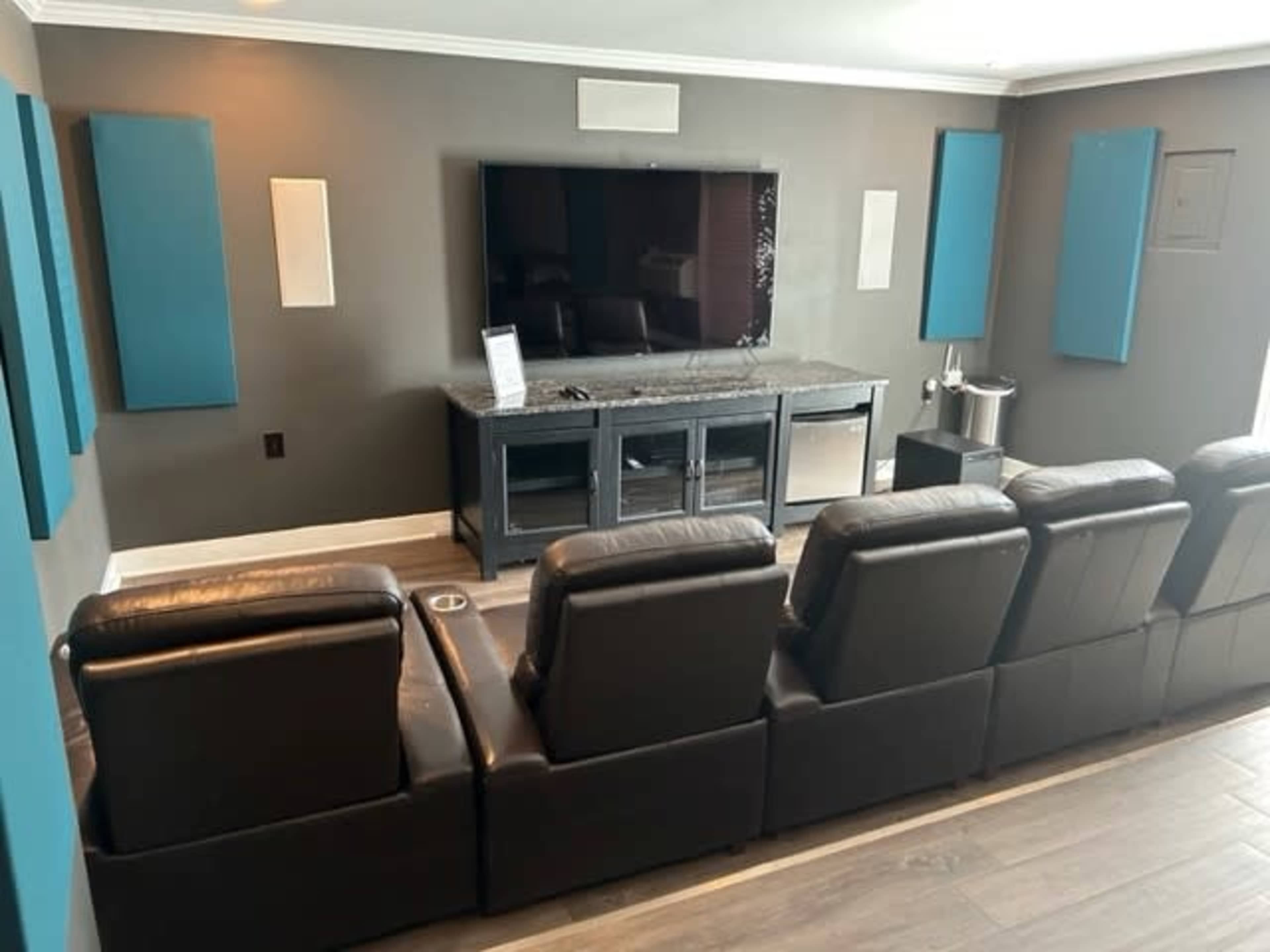 A home theater setup with a large television mounted on the wall, a dark media console, and row seating in front.