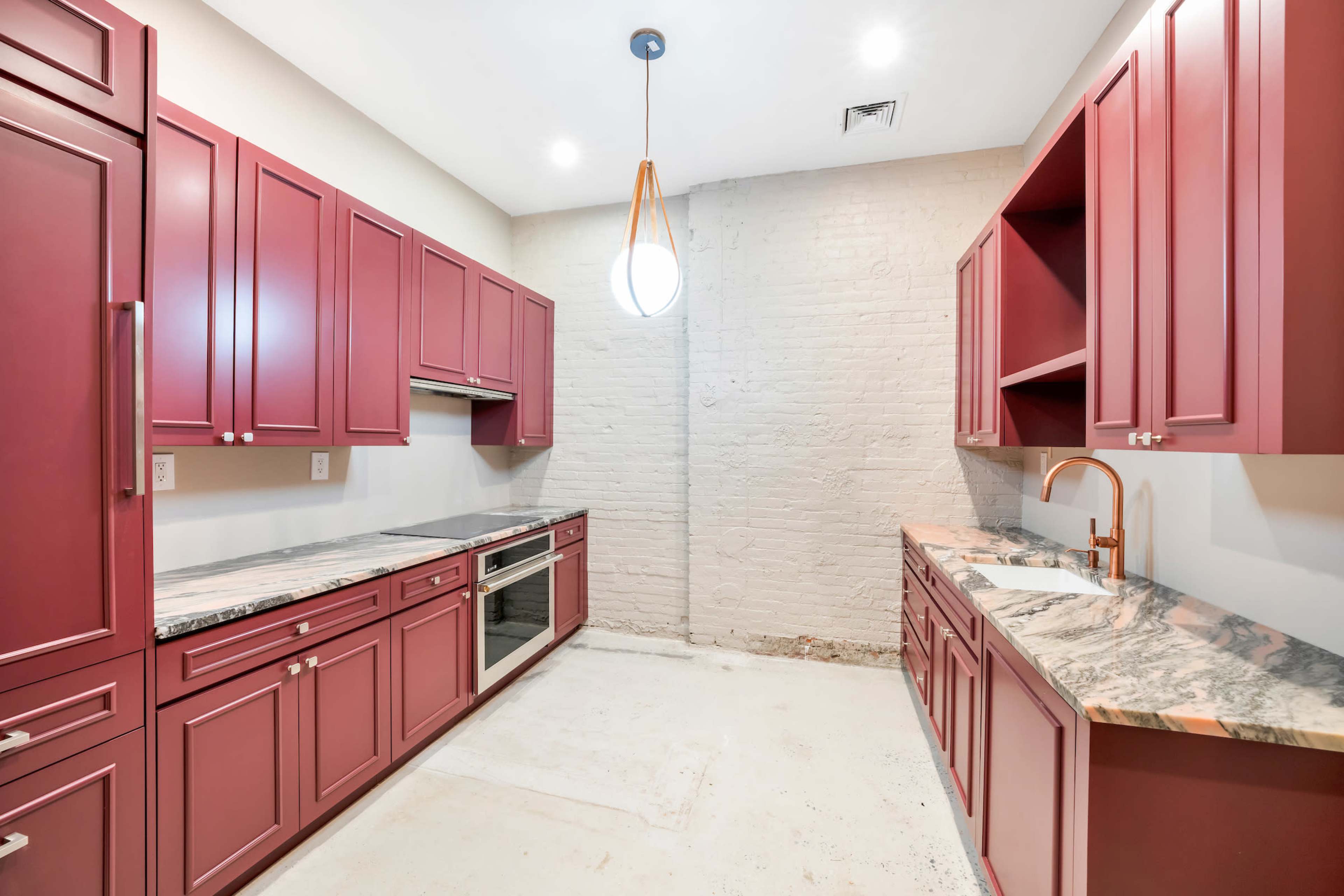 The image shows a kitchen with burgundy cabinets, marble countertops, and a single pendant light hanging from the ceiling.