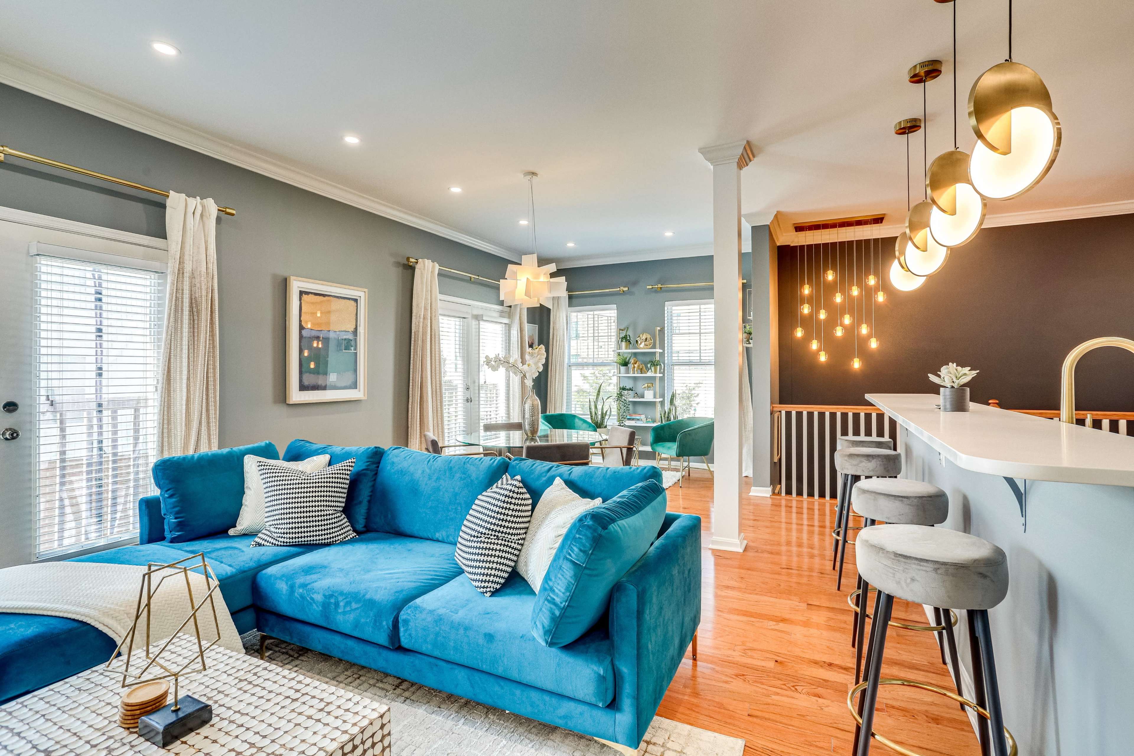 A modern living room with a blue sectional sofa, a light-colored rug, and a bar area with gold pendant lights.