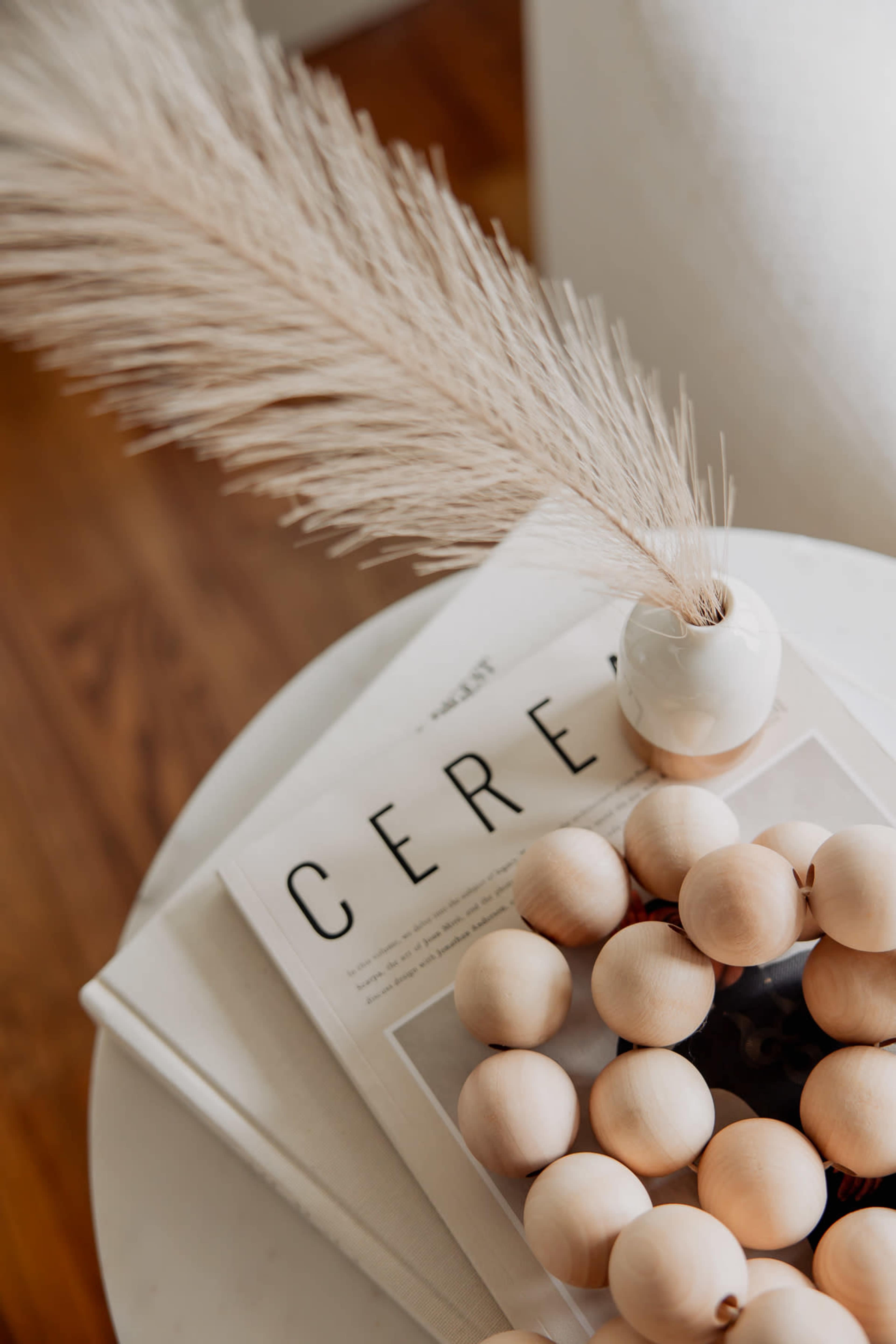 A decorative wooden bead arrangement sits on a stack of magazines beside a small vase with dried grass.