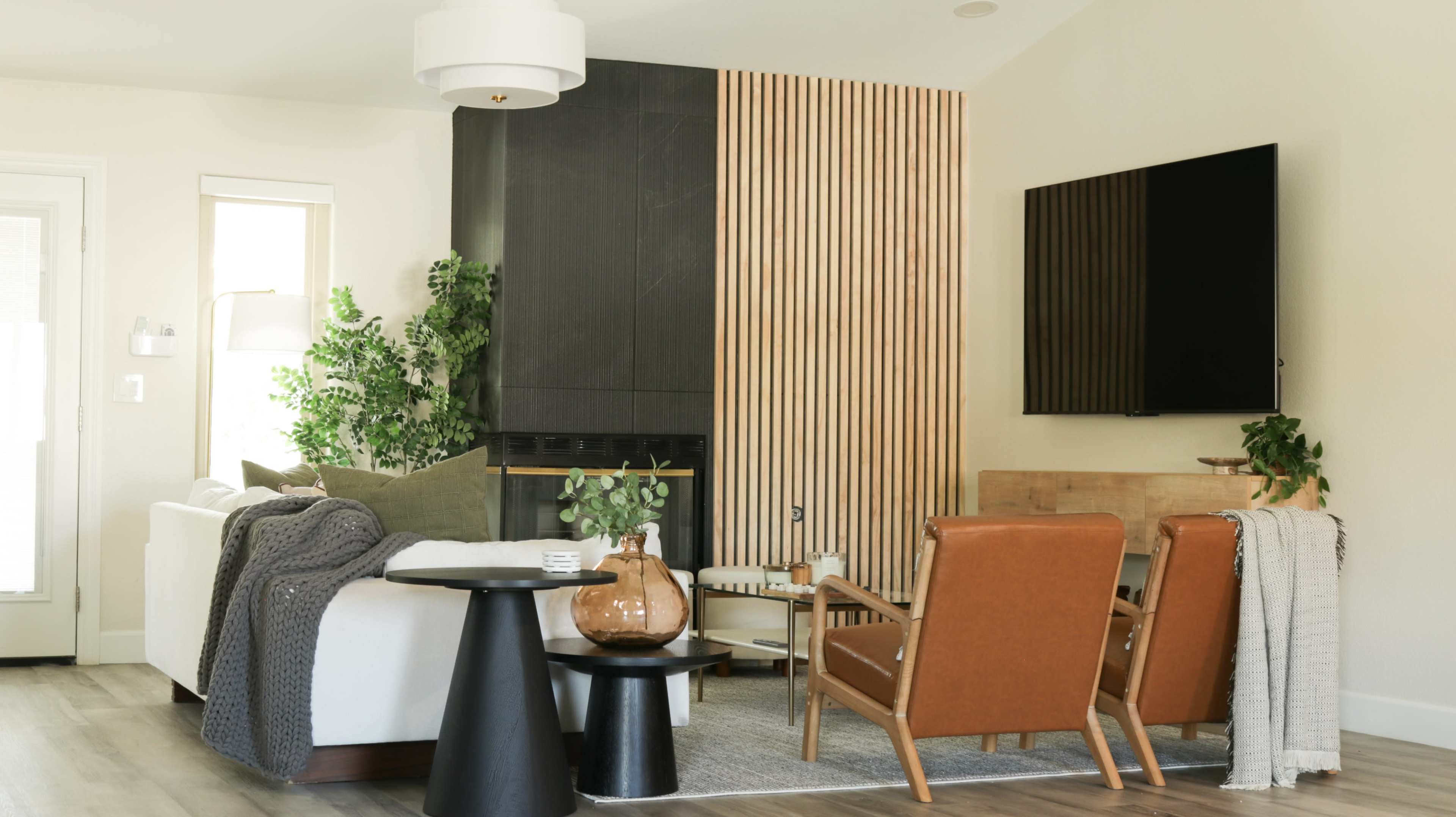 The living room features a modern design with a minimalist white sofa, brown leather chairs, a black side table, and a wooden accent wall.