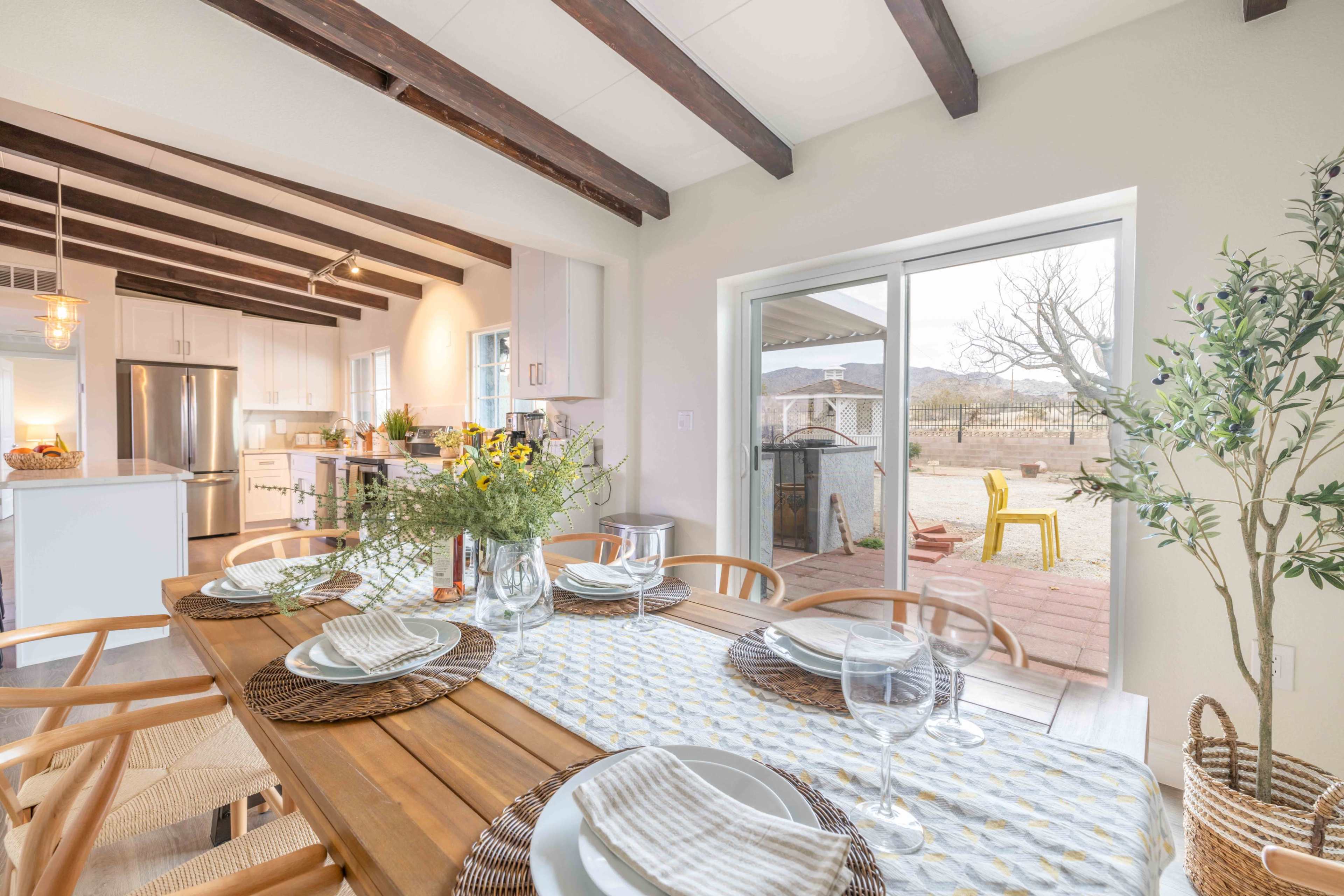 A dining table is set for a meal in a kitchen that opens to a outdoor view with mountains in the background.