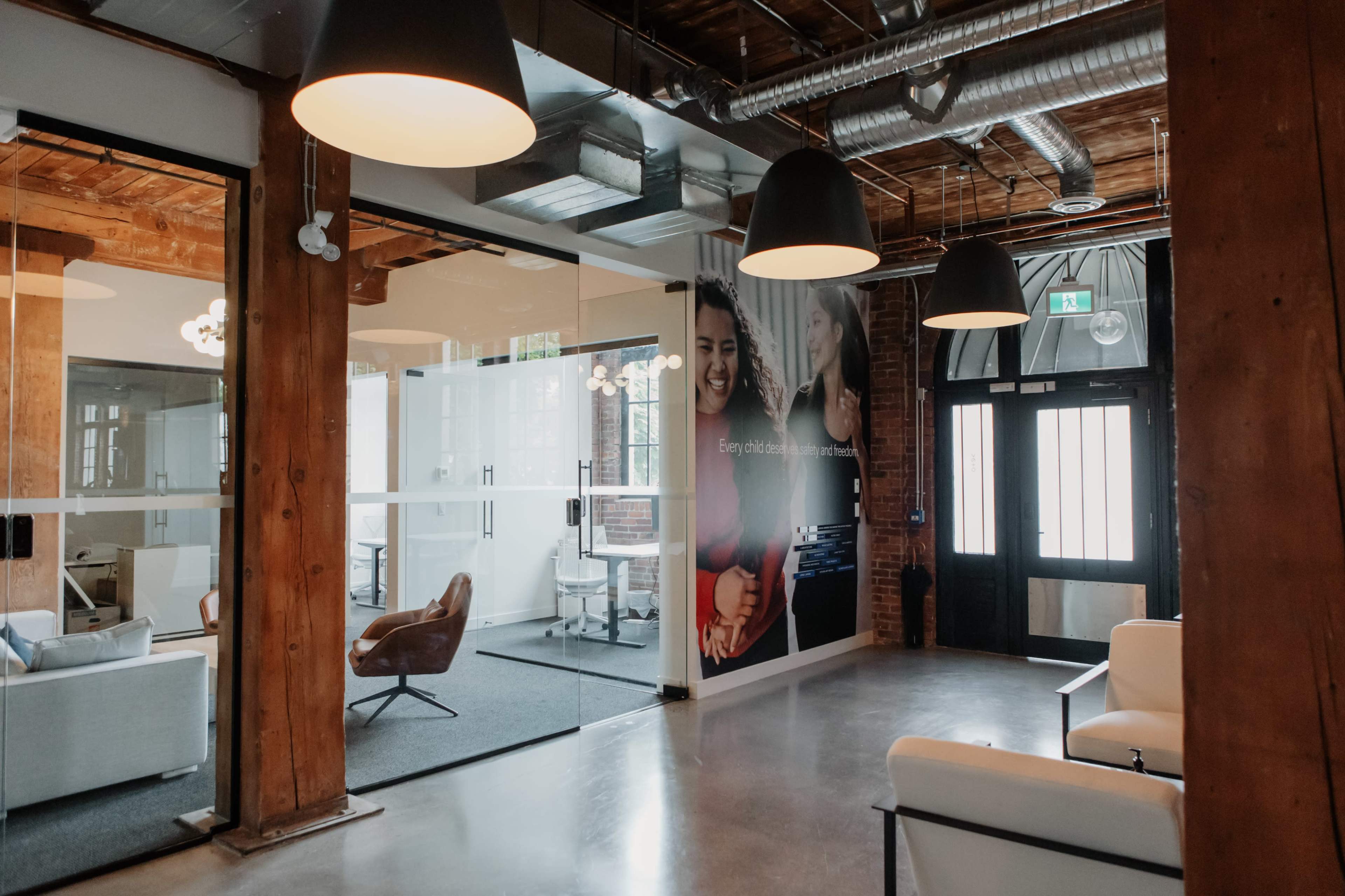 The image shows a modern office space with wooden beams, glass-paneled meeting rooms, and contemporary furniture.