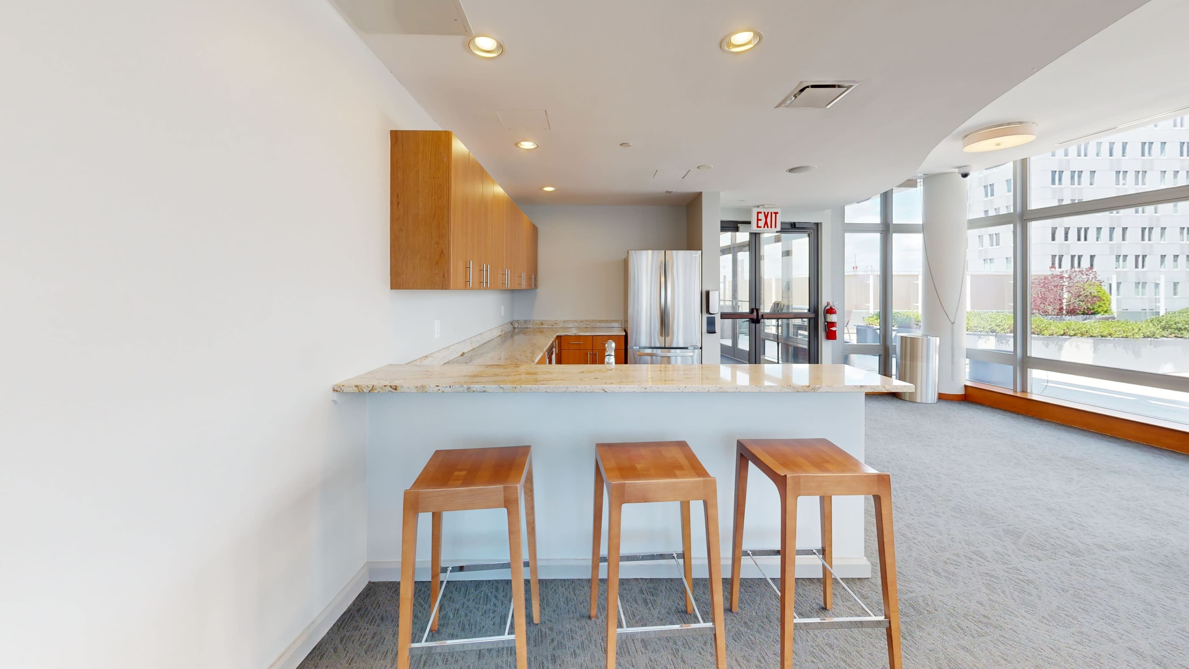 A modern kitchen area with a granite countertop and wooden bar stools, adjacent to large glass doors leading to an outdoor space.