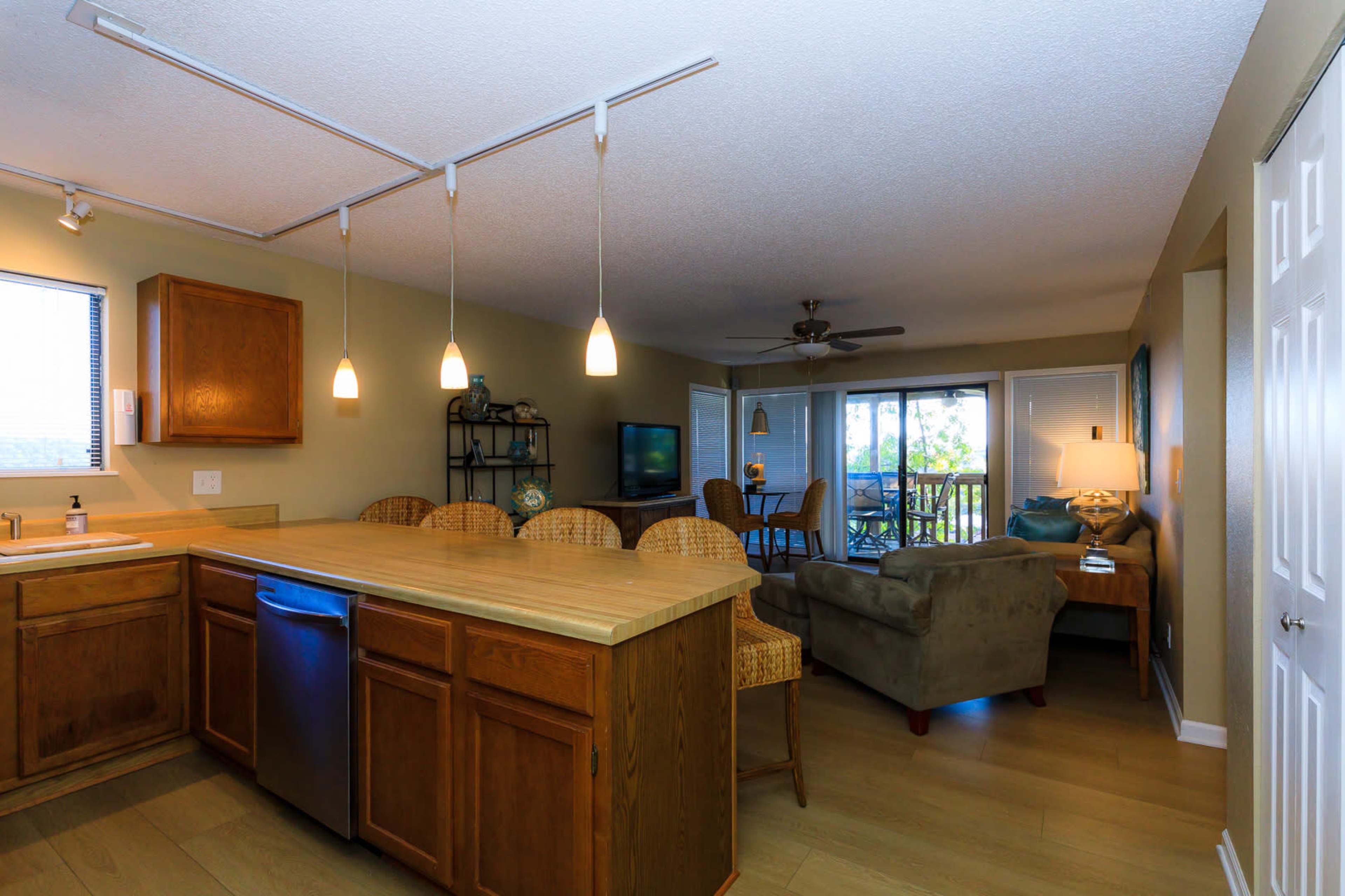An open-concept living area and kitchen with wooden cabinets, a countertop, and a seating area that leads to a balcony.