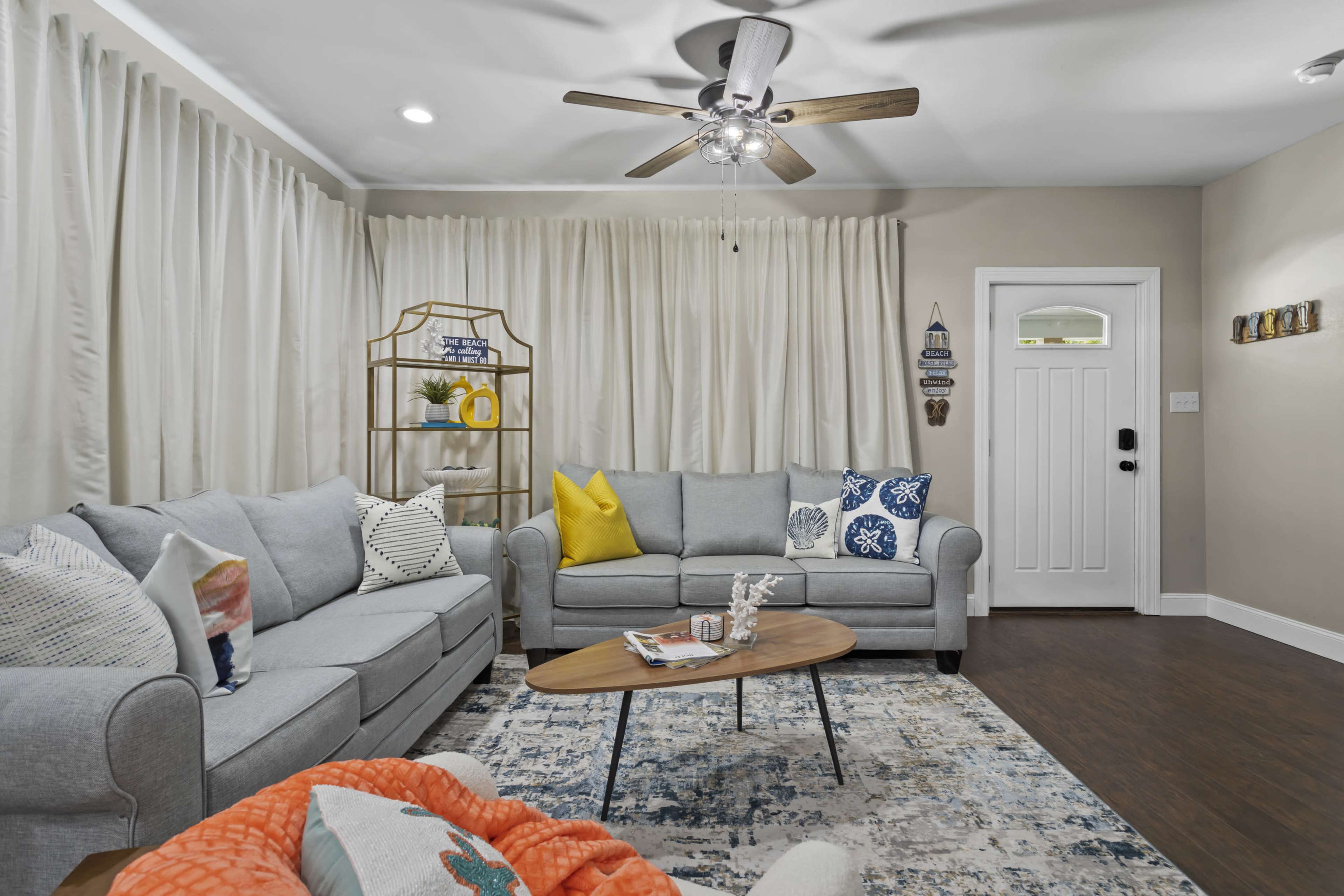 A cozy living room with a light gray sofa, an orange throw blanket, a wooden coffee table, and a white door with a glass panel.