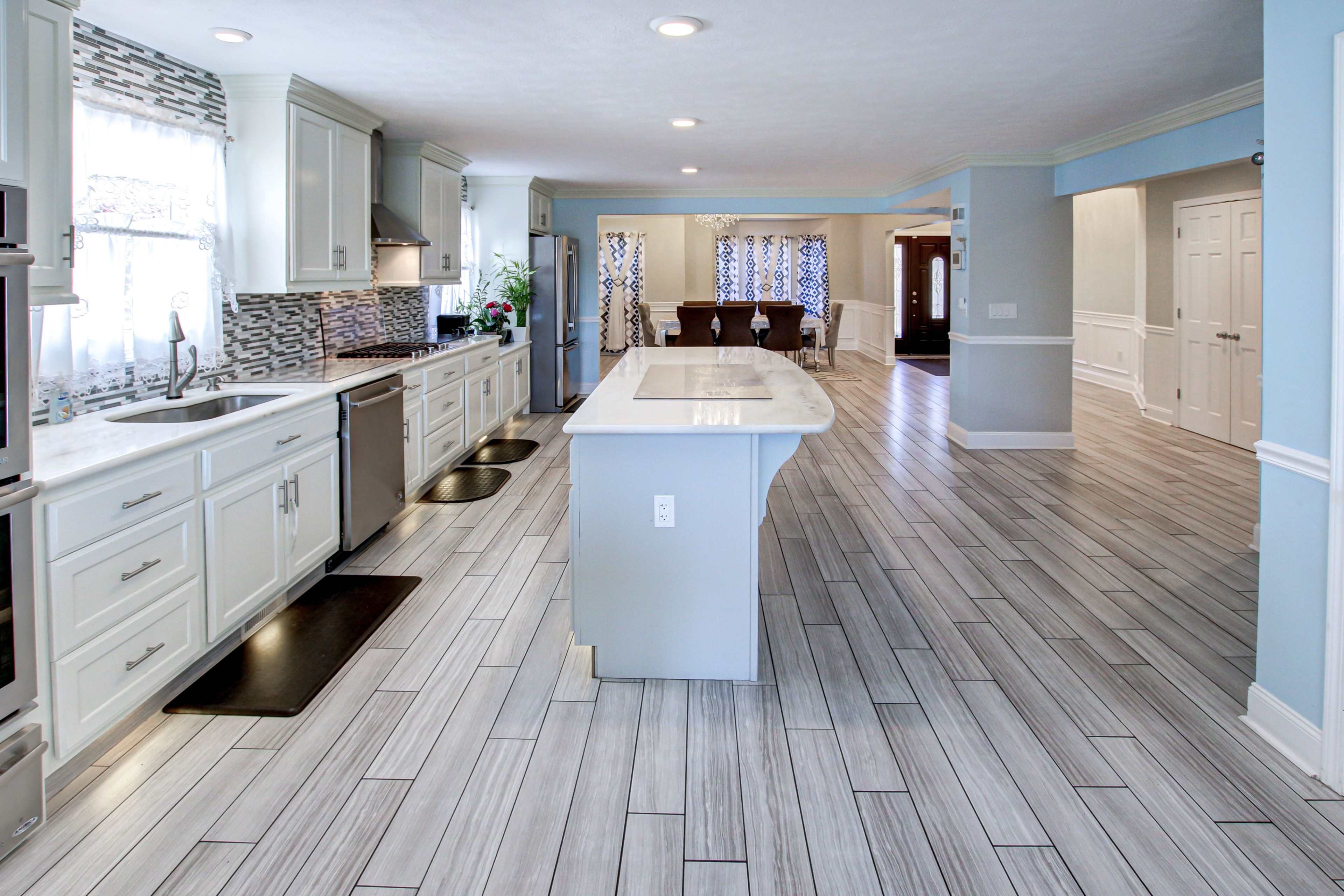 A spacious kitchen with white cabinets, stainless steel appliances, and a large central island, leading to an adjacent dining area with a table and chairs.