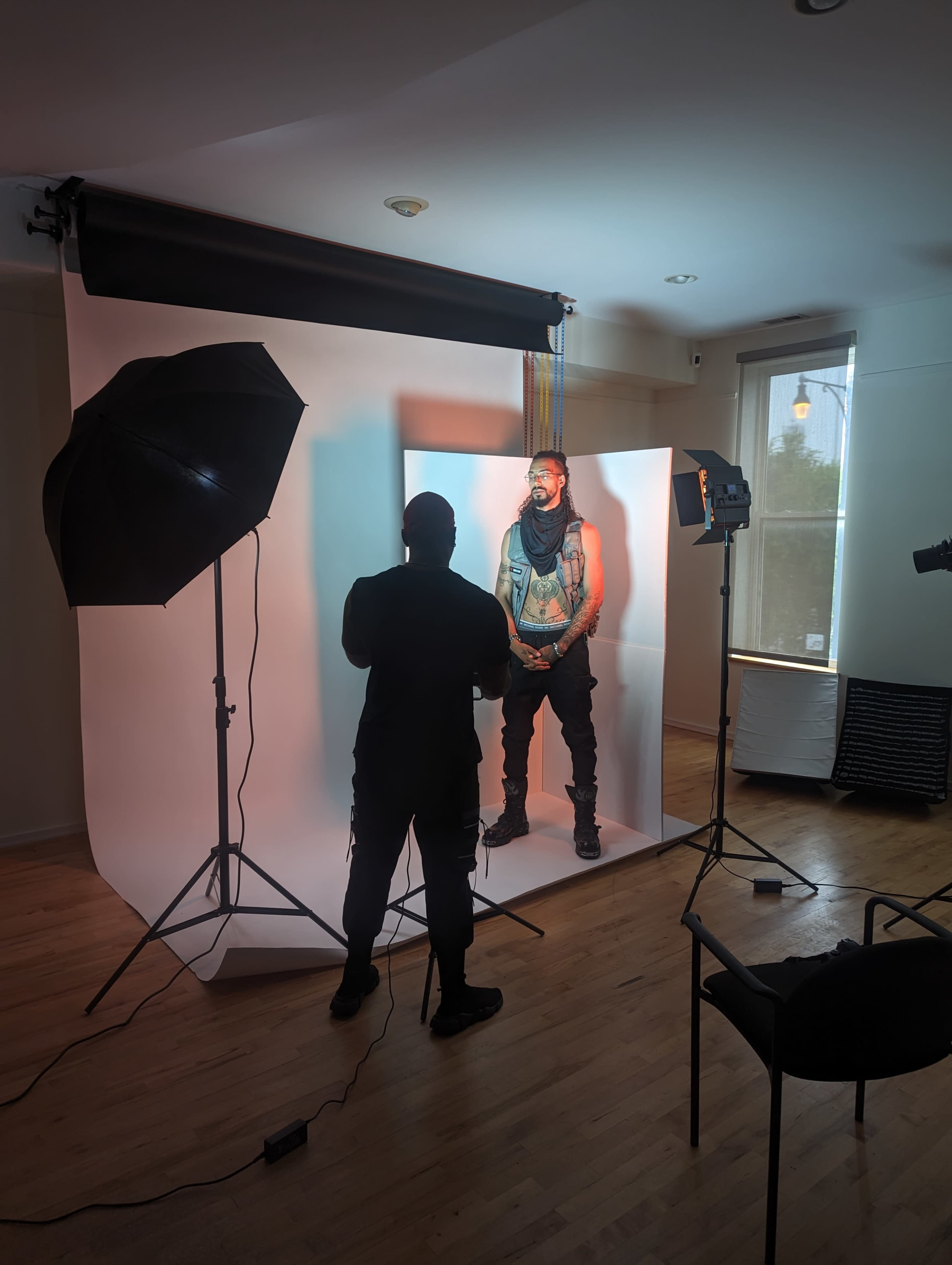A photographer is capturing an image of a model standing against a white backdrop in a well-lit studio.