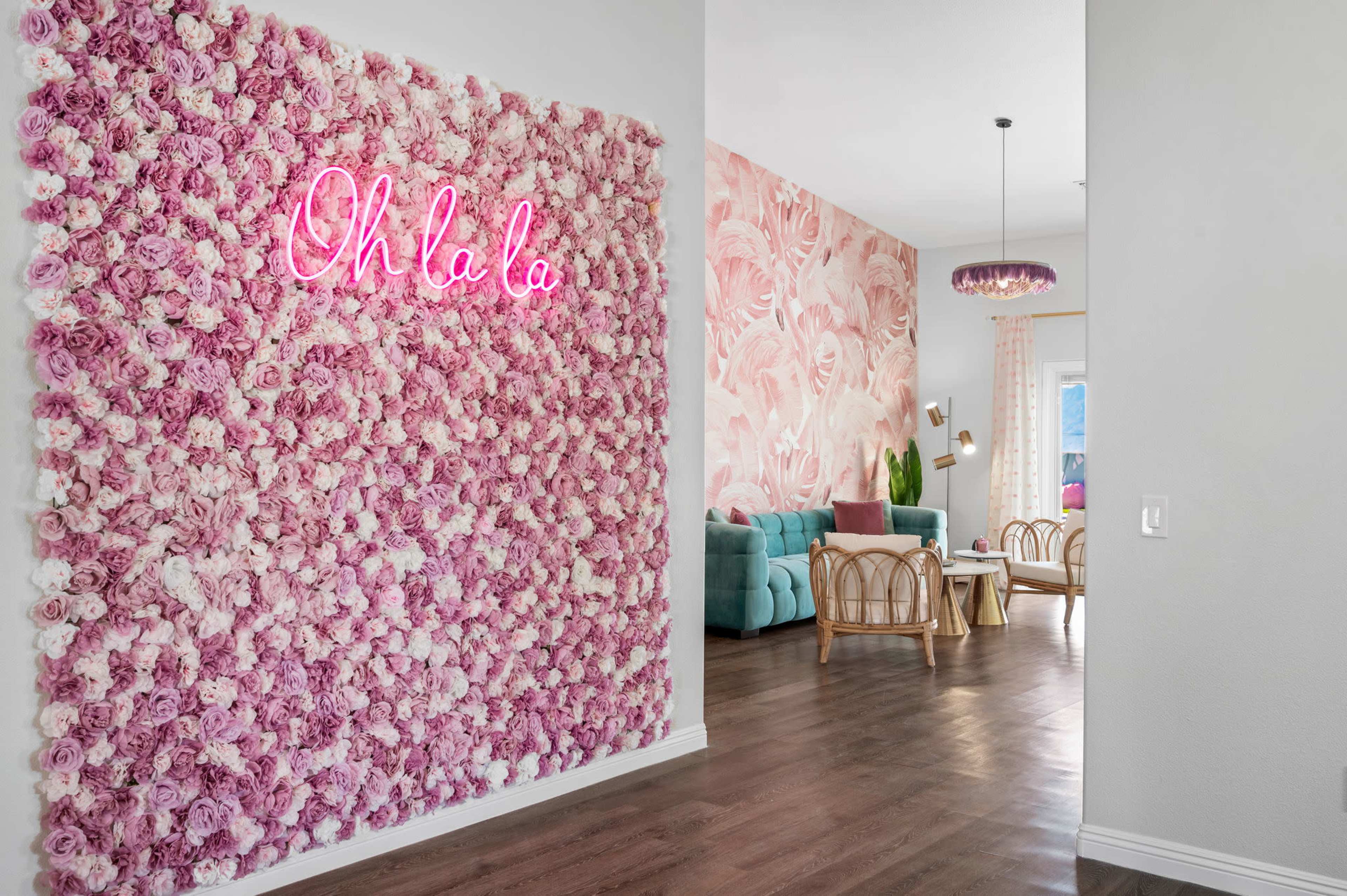 A hallway features a floral wall with a neon sign that says "Oh la la," leading to a living area with pastel furnishings and floral wallpaper.