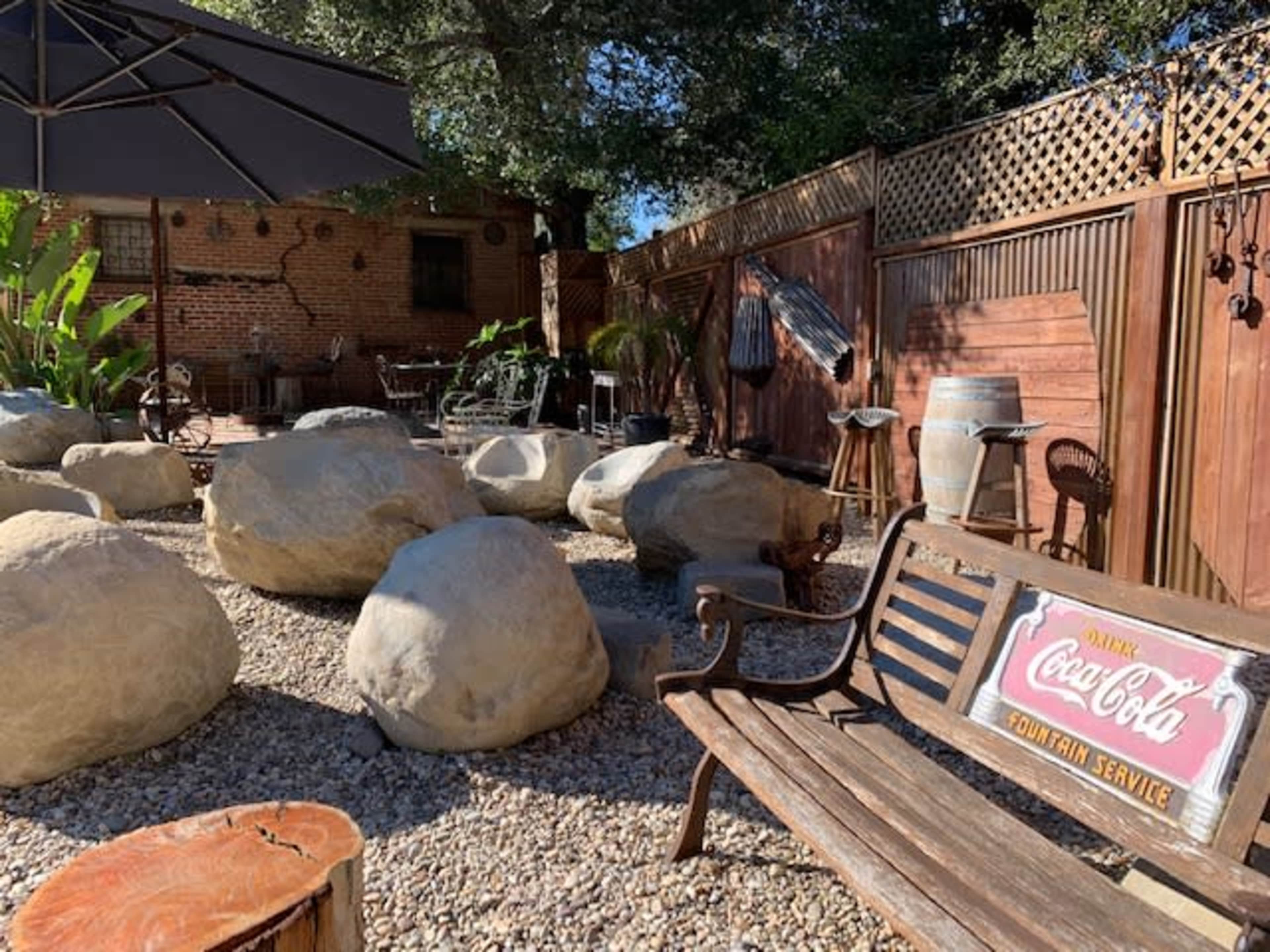 A patio area features large rock formations surrounded by gravel, rustic furniture, and a vintage Coca-Cola sign.