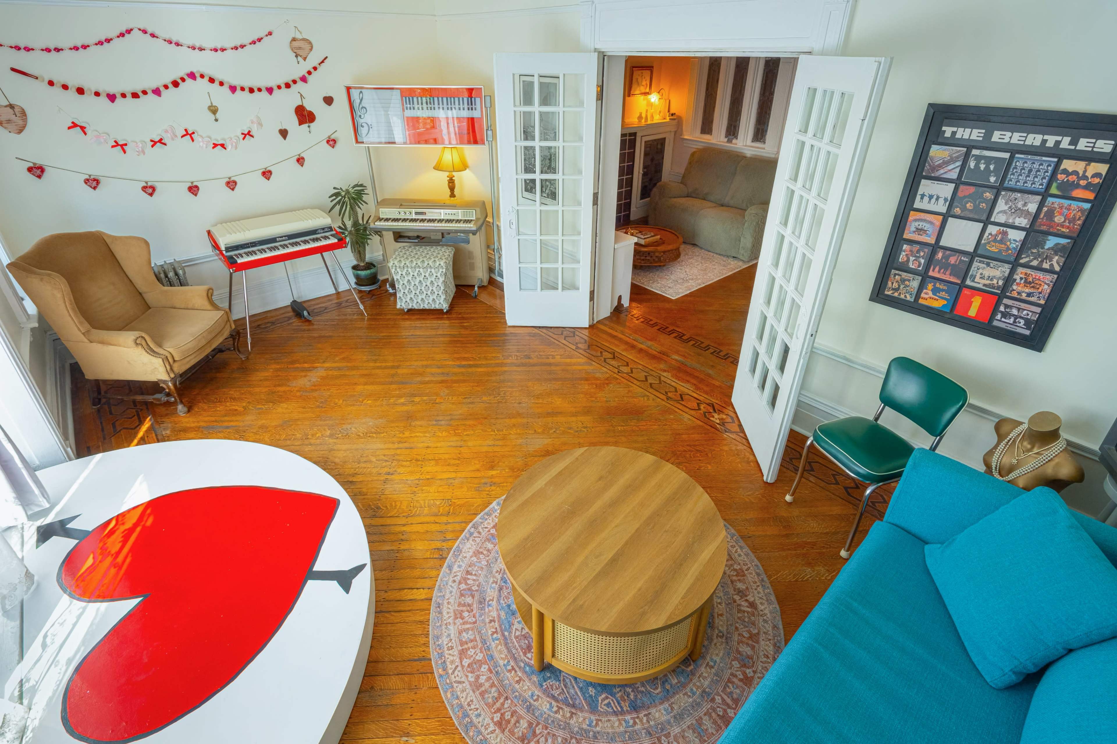 The image shows a cozy living room with hardwood floors, a large heart-shaped coffee table, a blue couch, and decorative wall art, including a red and white theme.