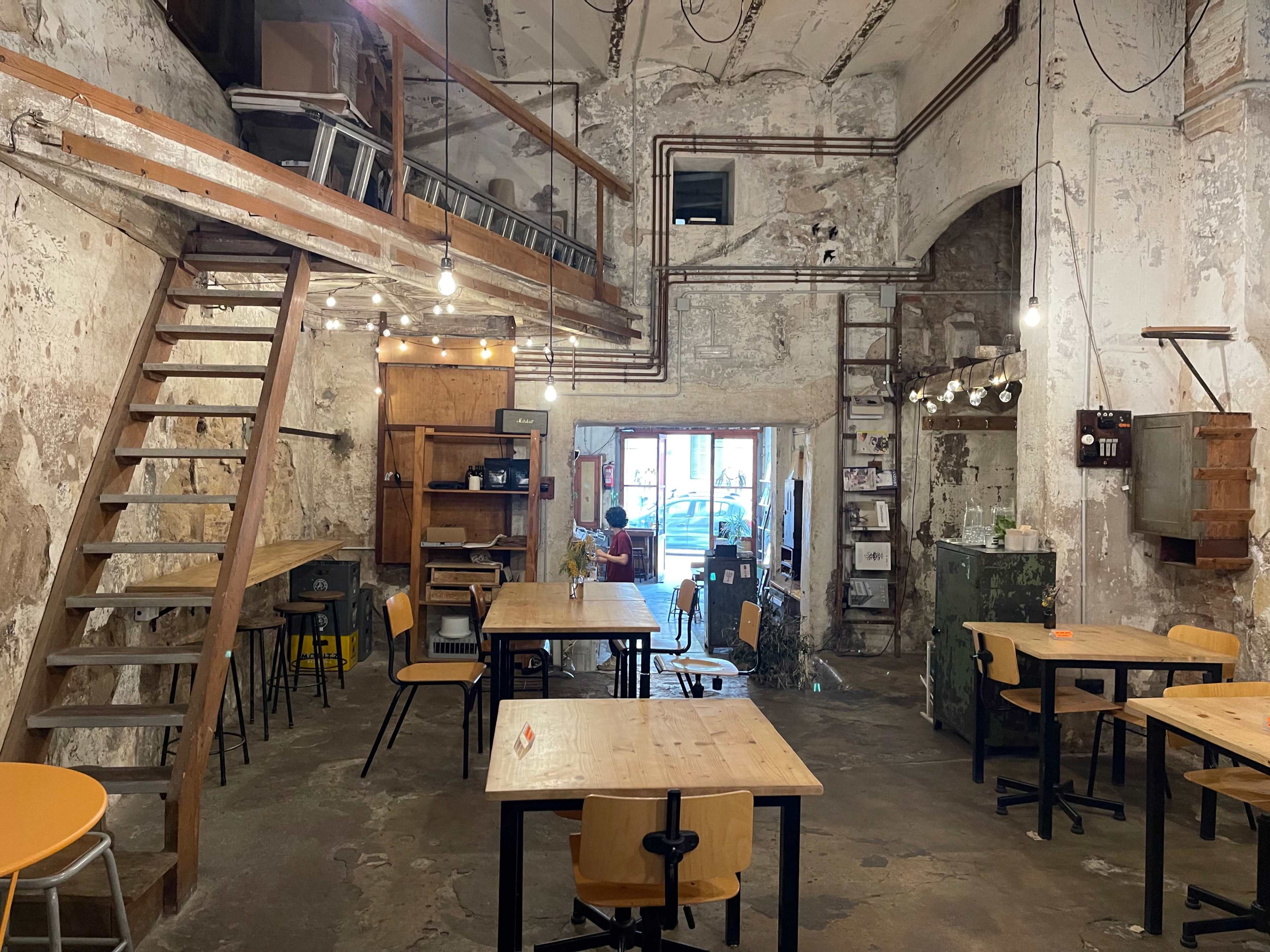 An interior of a rustic café with wooden tables, chairs, and a staircase leading to a lofted area.