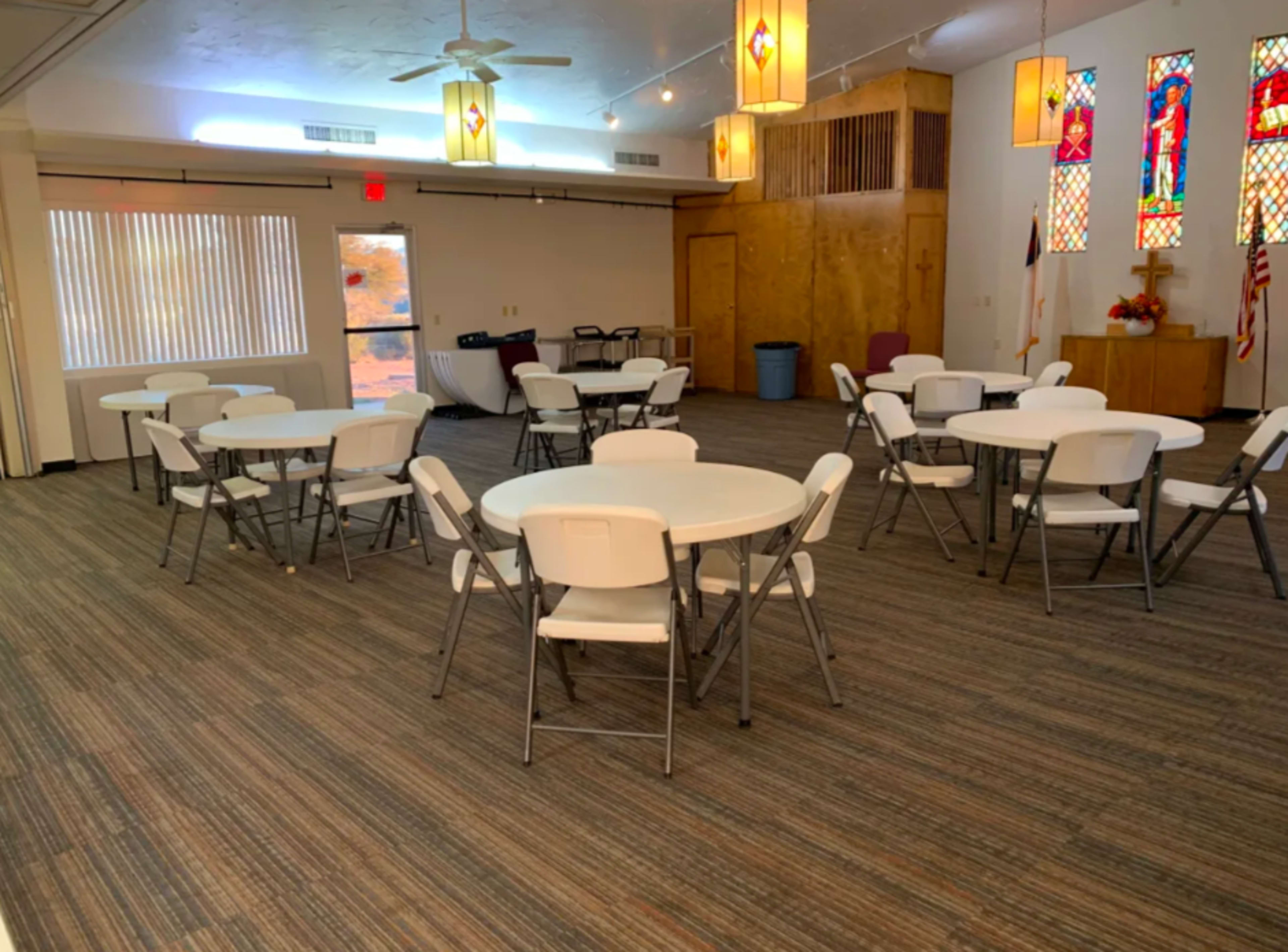 A spacious room arranged with several round tables and chairs, complemented by stained glass windows and light fixtures.