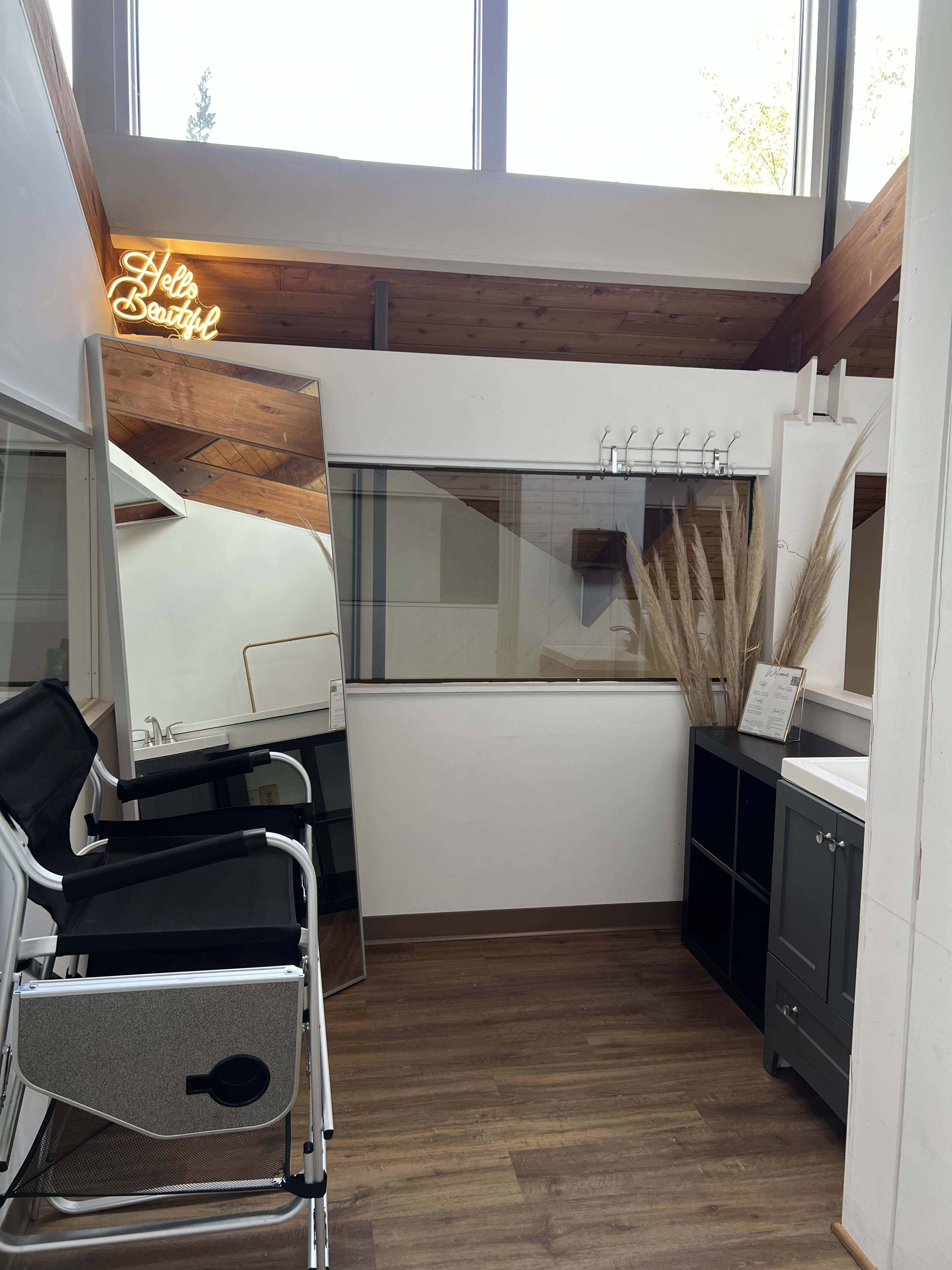 A bright salon interior features a large mirror, a stylist chair, and decorative elements including a plant and a sign.