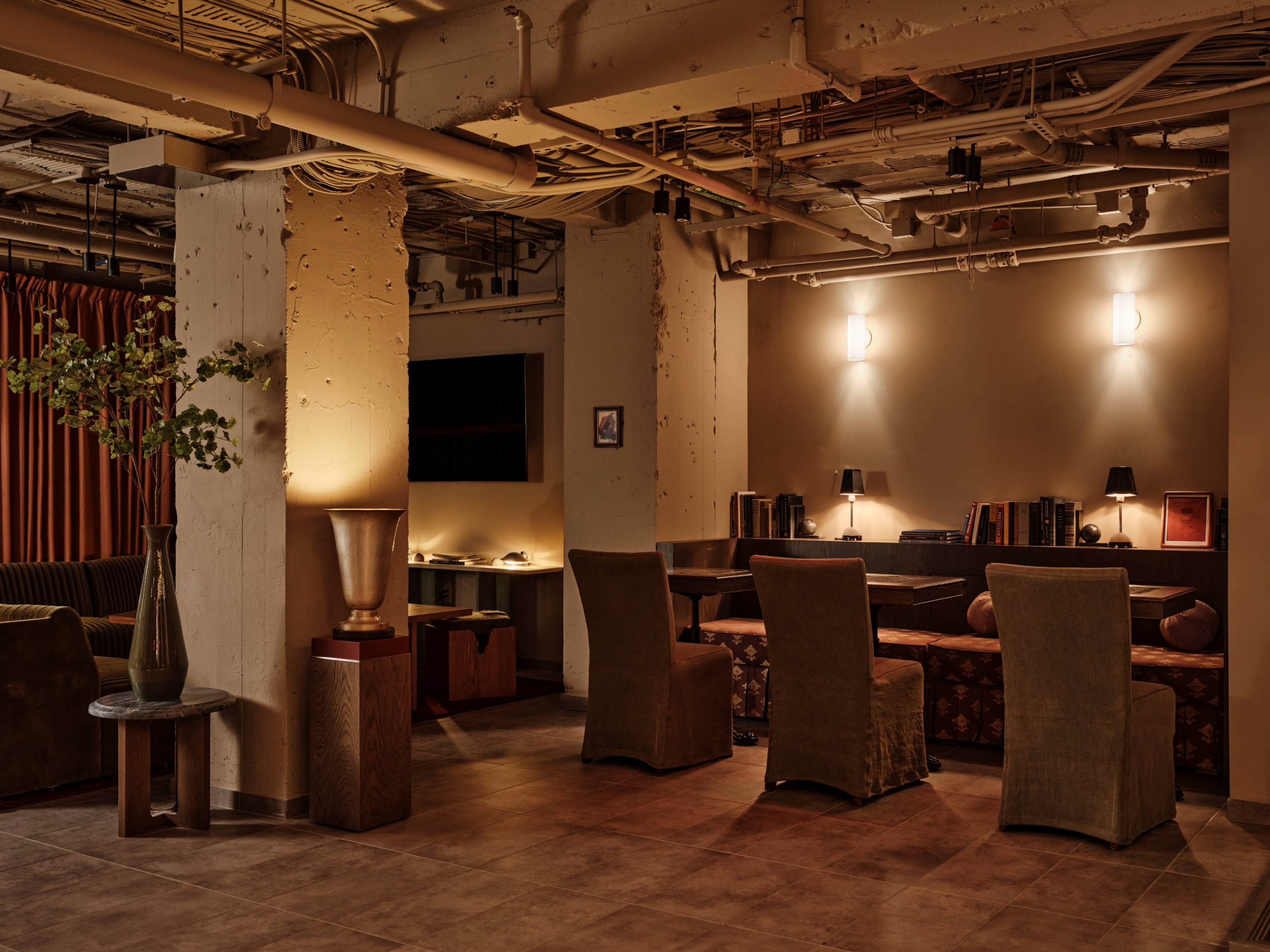The image depicts a dimly lit lounge area featuring textured walls, various seating options, and ambient lighting.