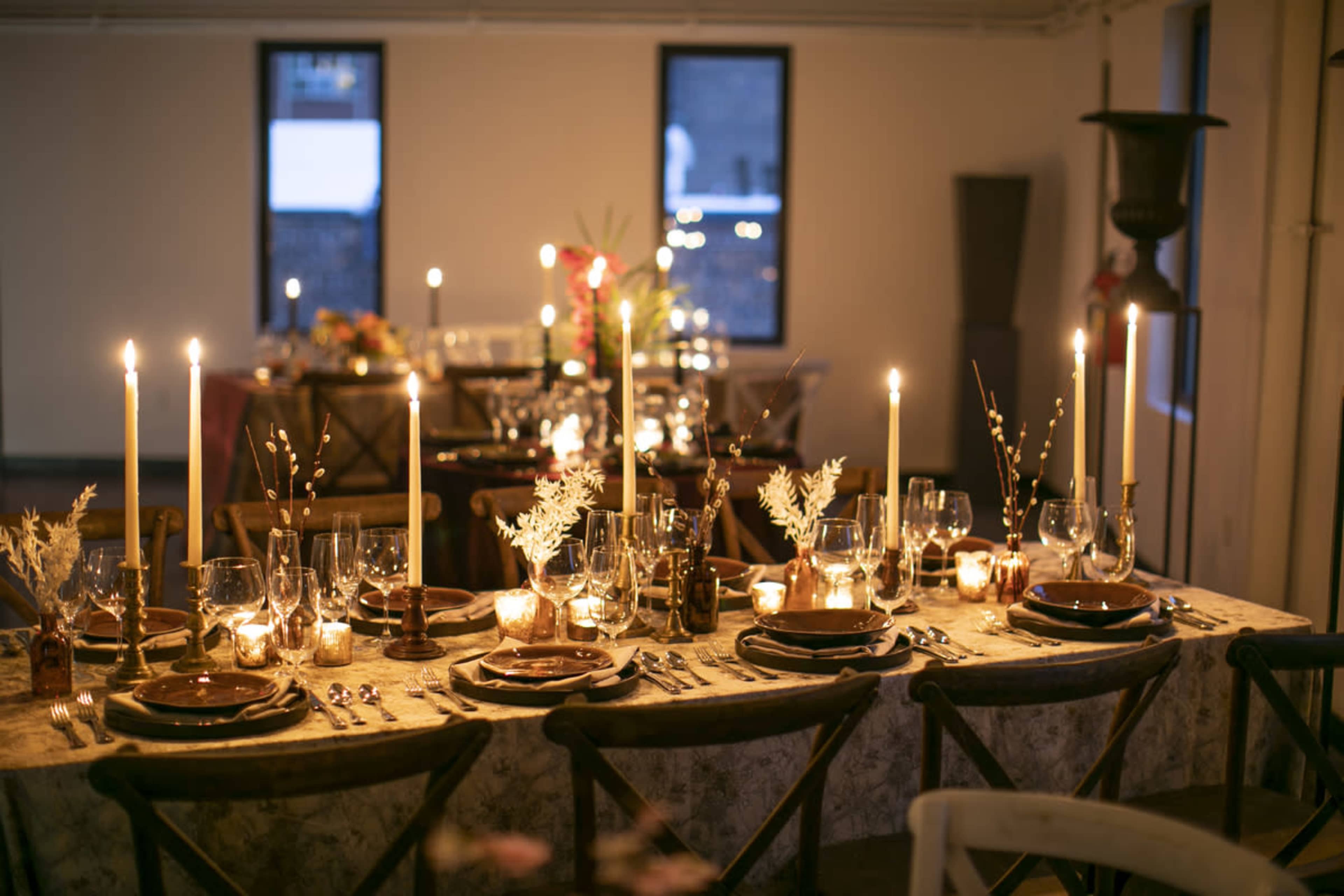 A elegantly set dining table with candles, glassware, and floral arrangements is illuminated in a warmly lit banquet hall.