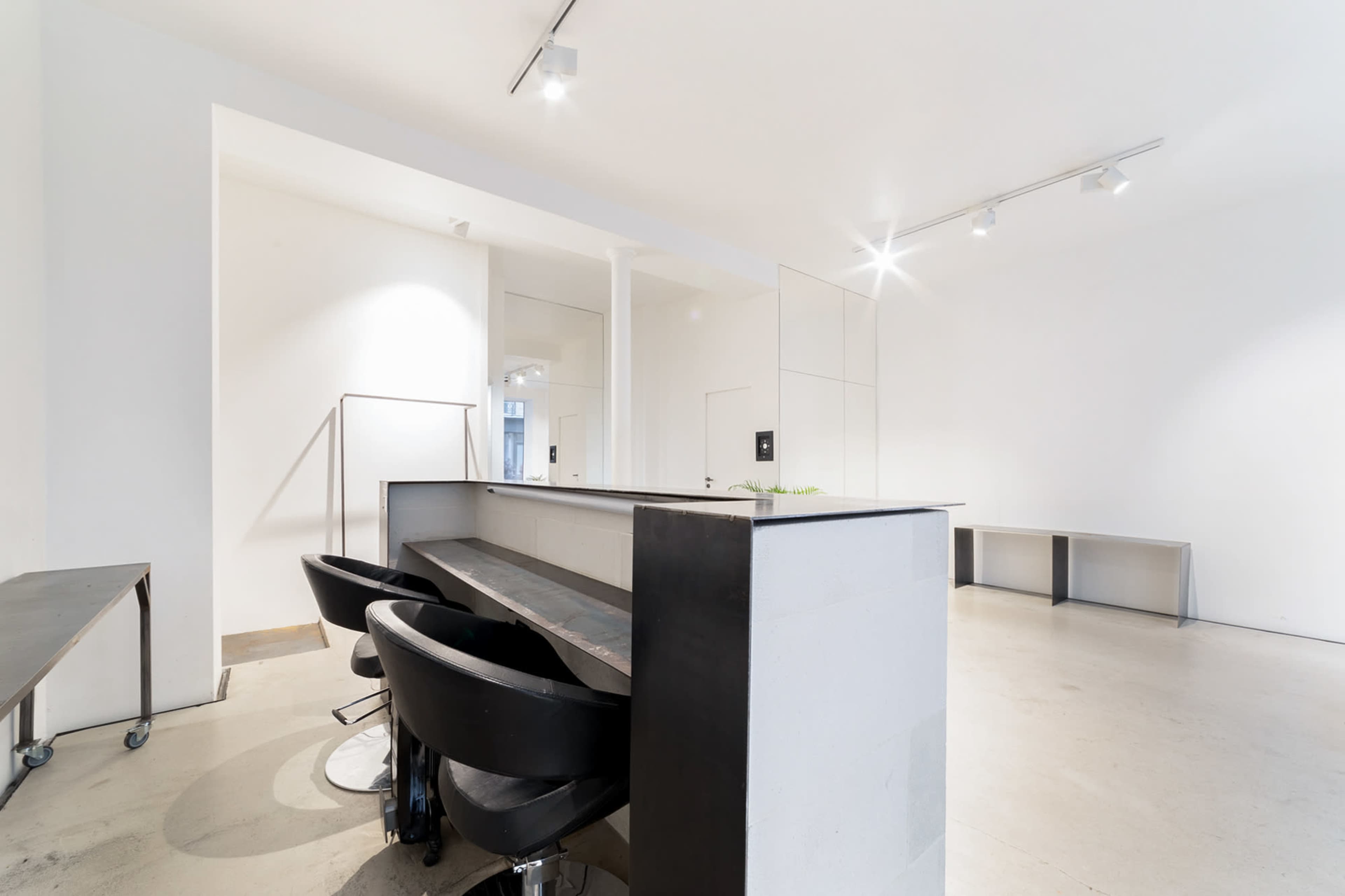 A minimalistic interior features a bar counter with black stools, white walls, and modern lighting.
