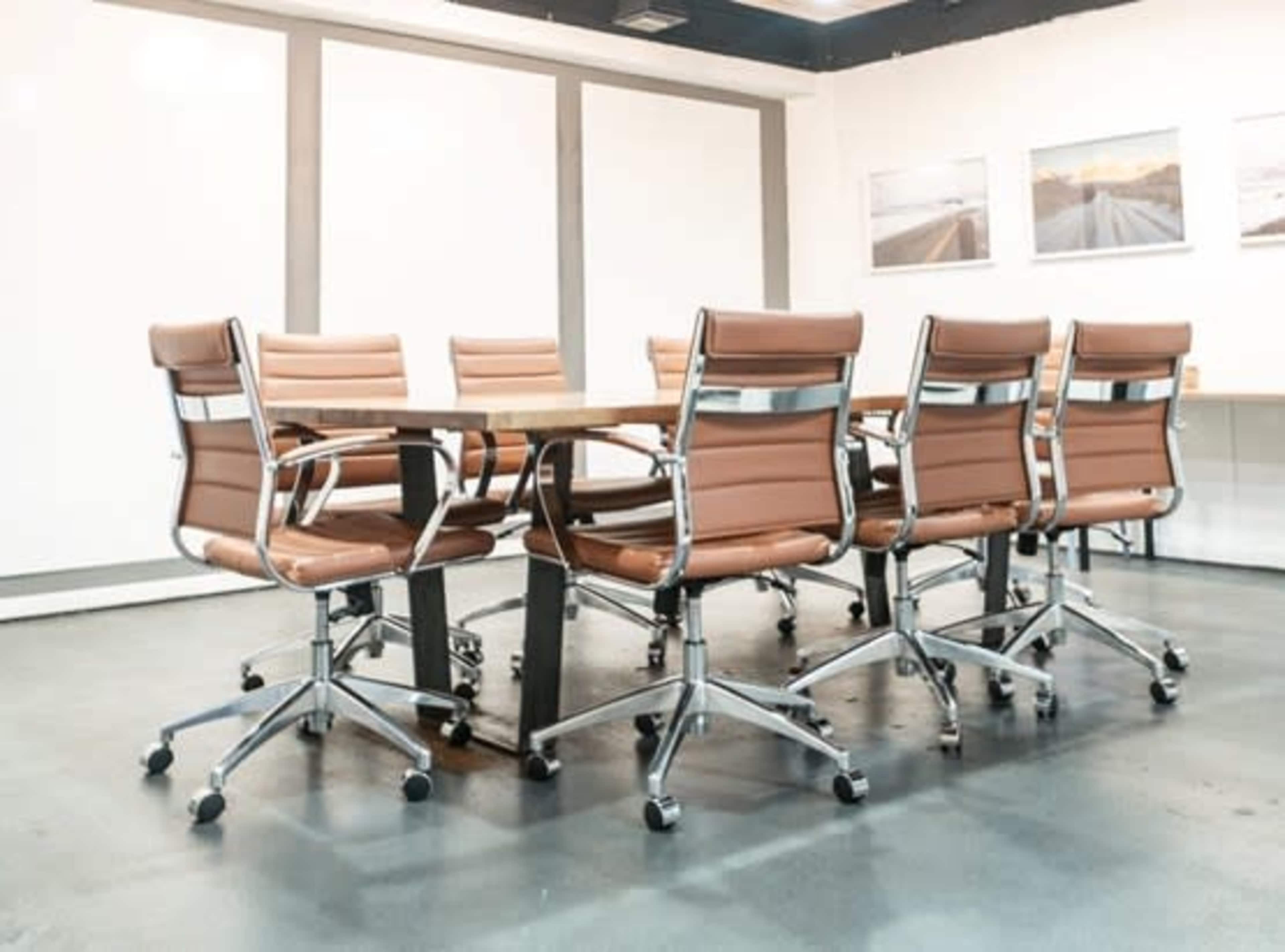 A modern conference room features a large table surrounded by ergonomic chairs with brown leather upholstery.