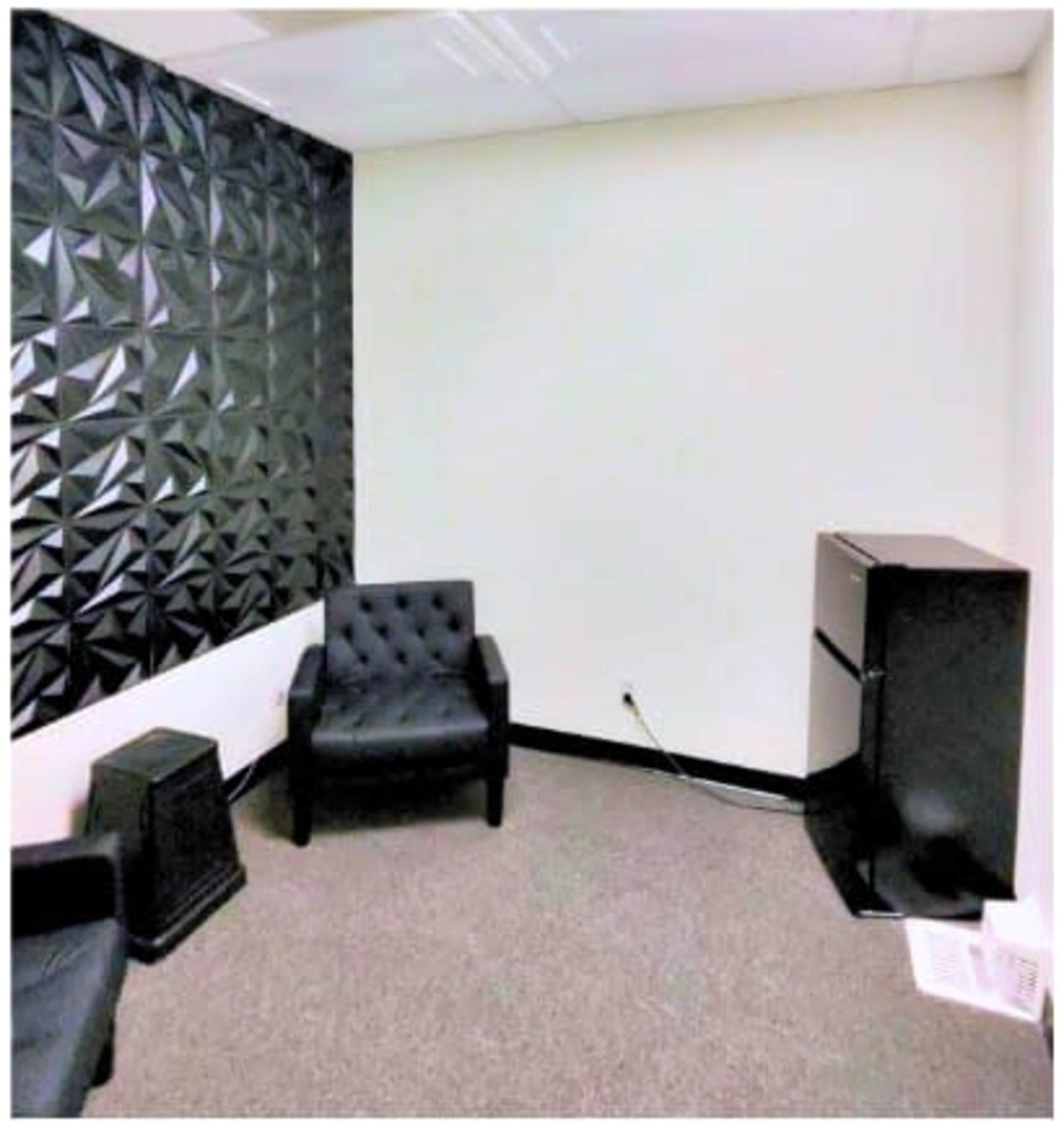 The image shows a small room with two black chairs, a black mini-fridge, and a textured black wall.