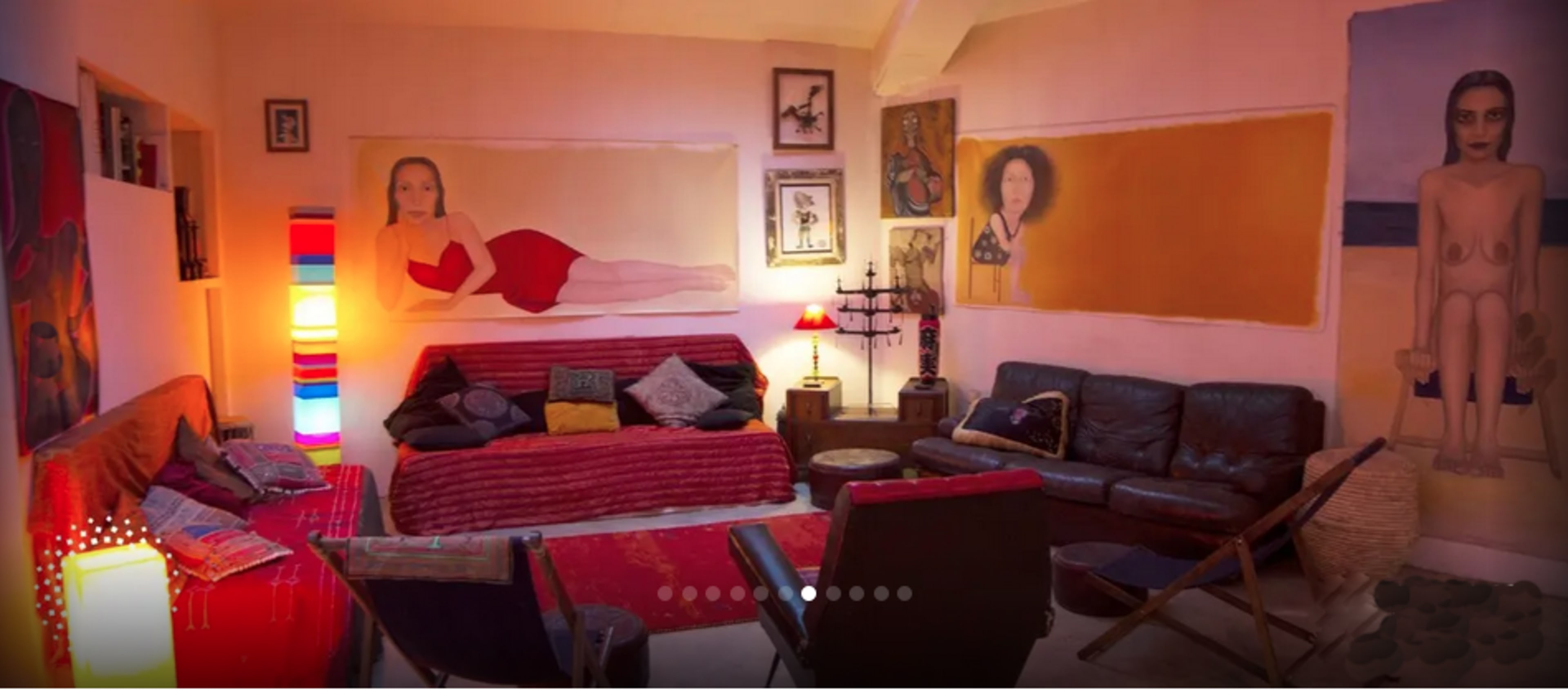 The room features a colorful seating area with a red bedspread and large artwork on the walls.