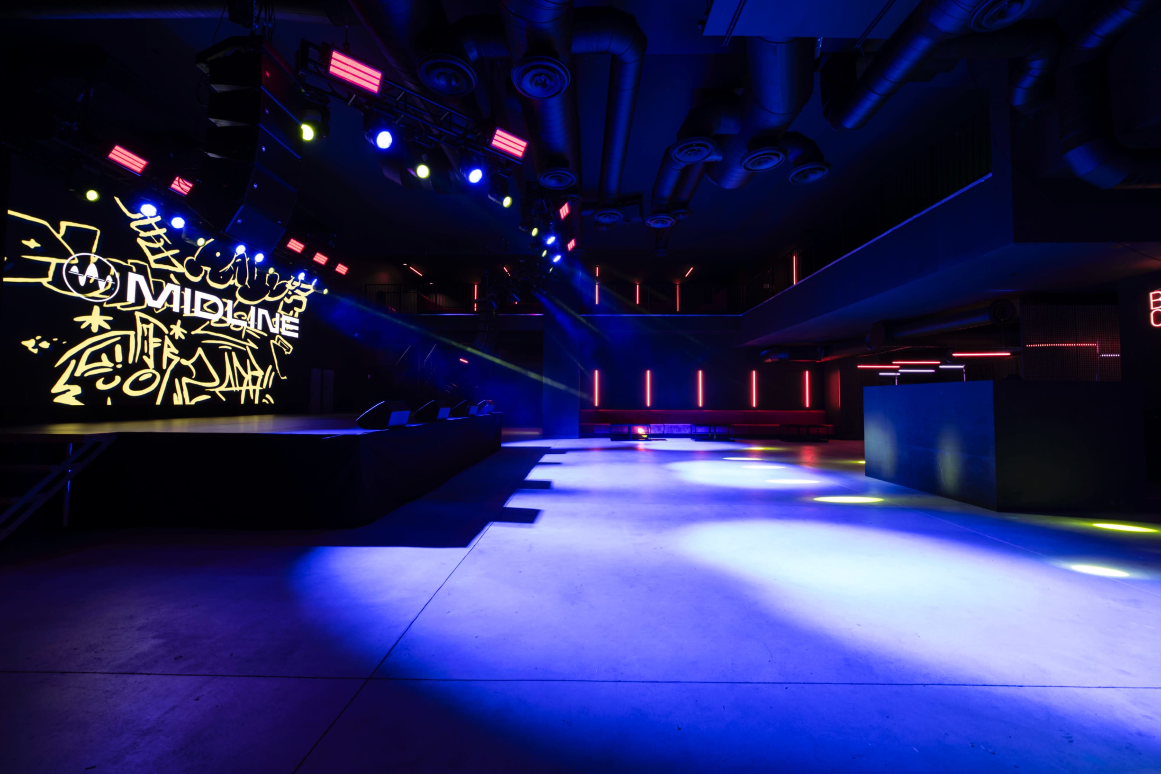 The image shows a dimly lit nightclub interior with colorful stage lights, graffiti-style art on the wall, and an empty dance floor.