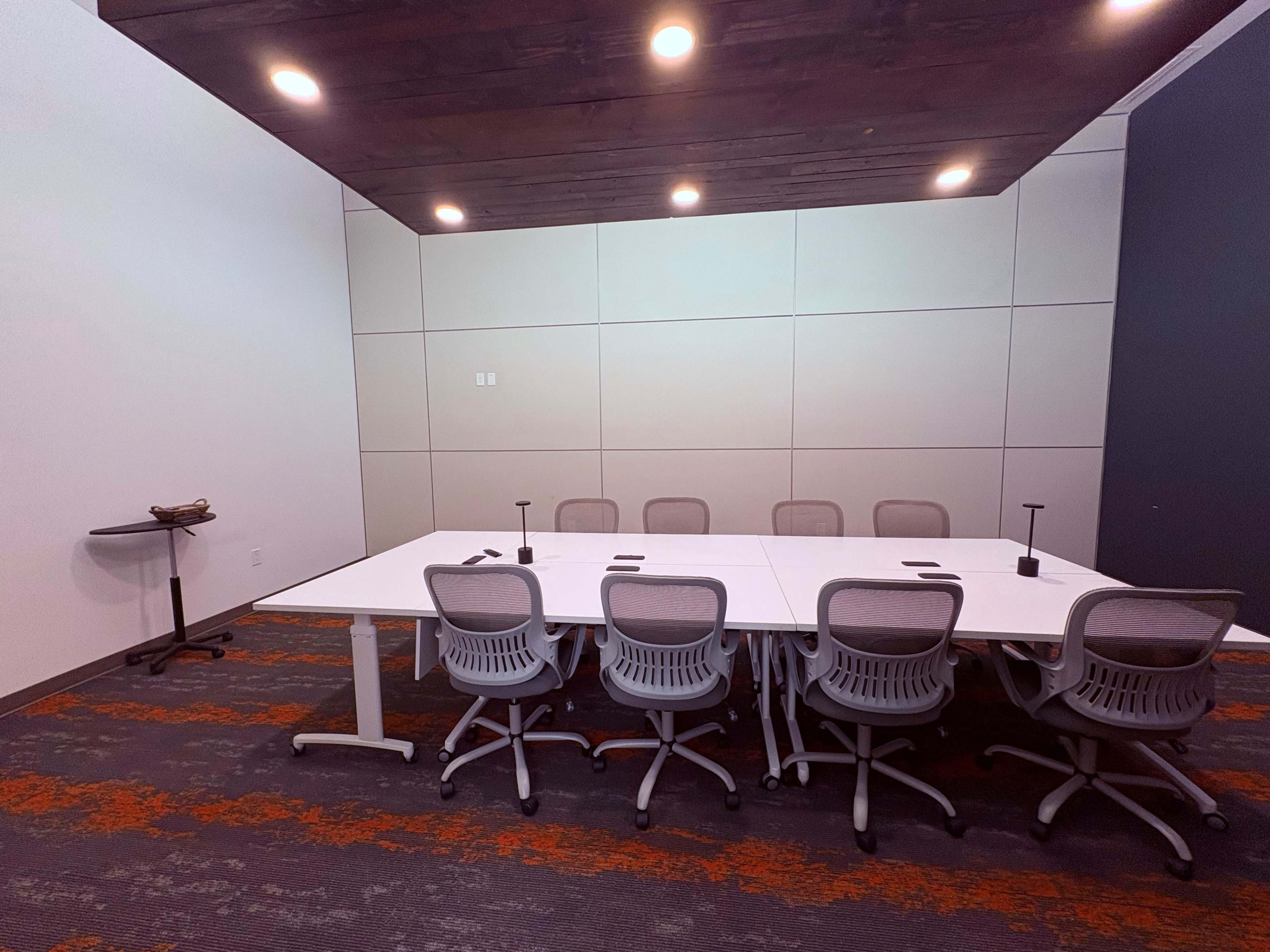 A conference room features a large white table surrounded by several ergonomic chairs, with modern lighting above.