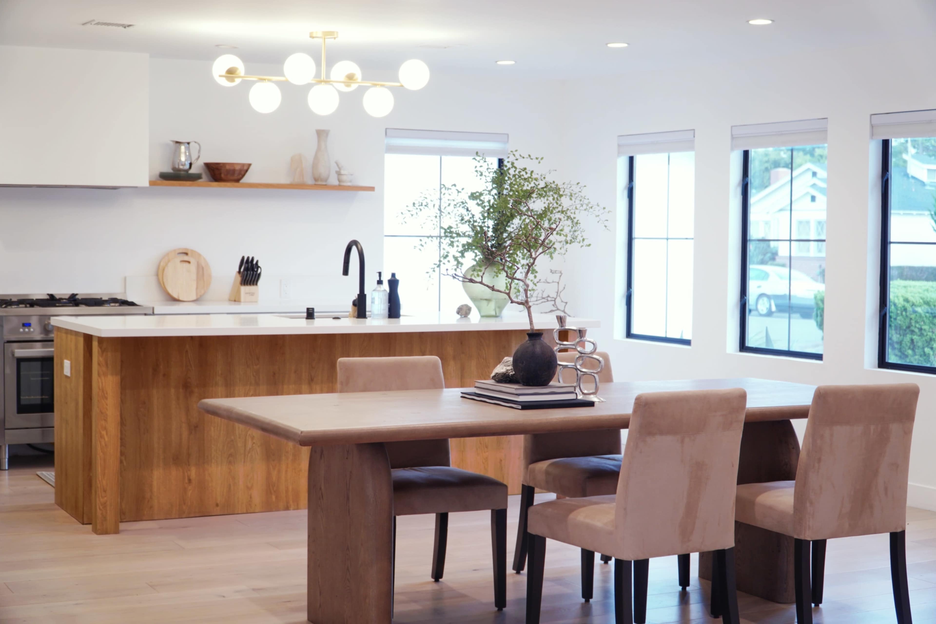 A dining area features a wooden table surrounded by four chairs, with a modern kitchen visible in the background.