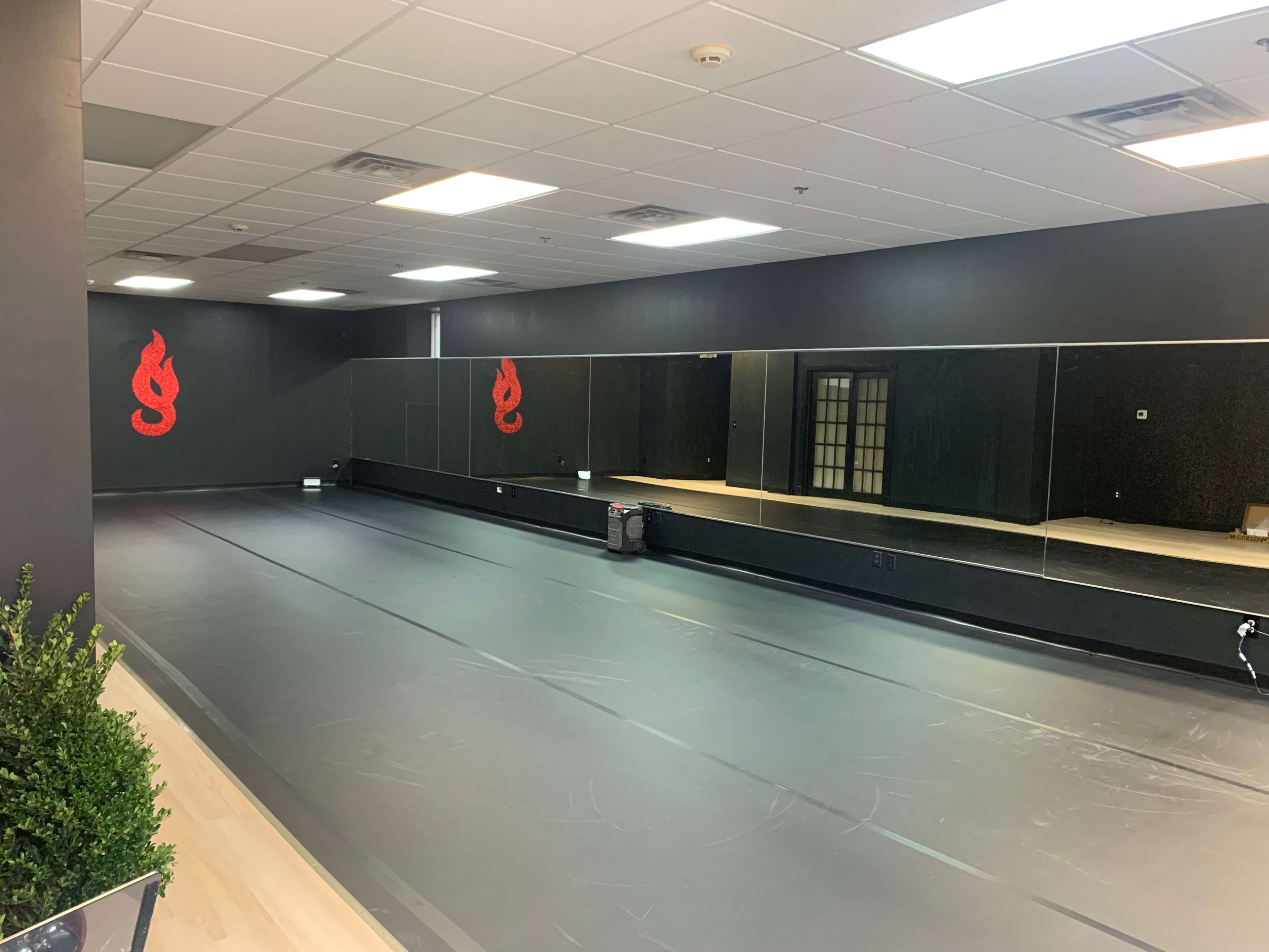 An empty dance studio with a black floor and mirrored walls, featuring red decorative elements.