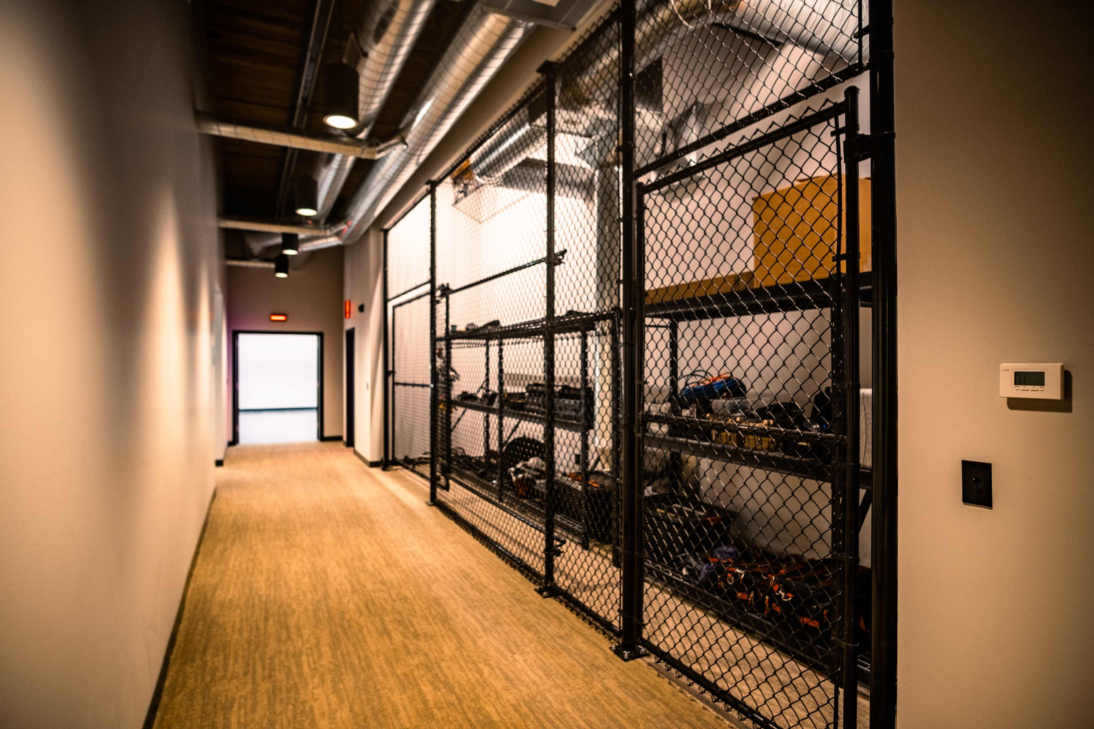 A narrow hallway with a chain-link fence and metal shelving units along one side, stacked with various items.