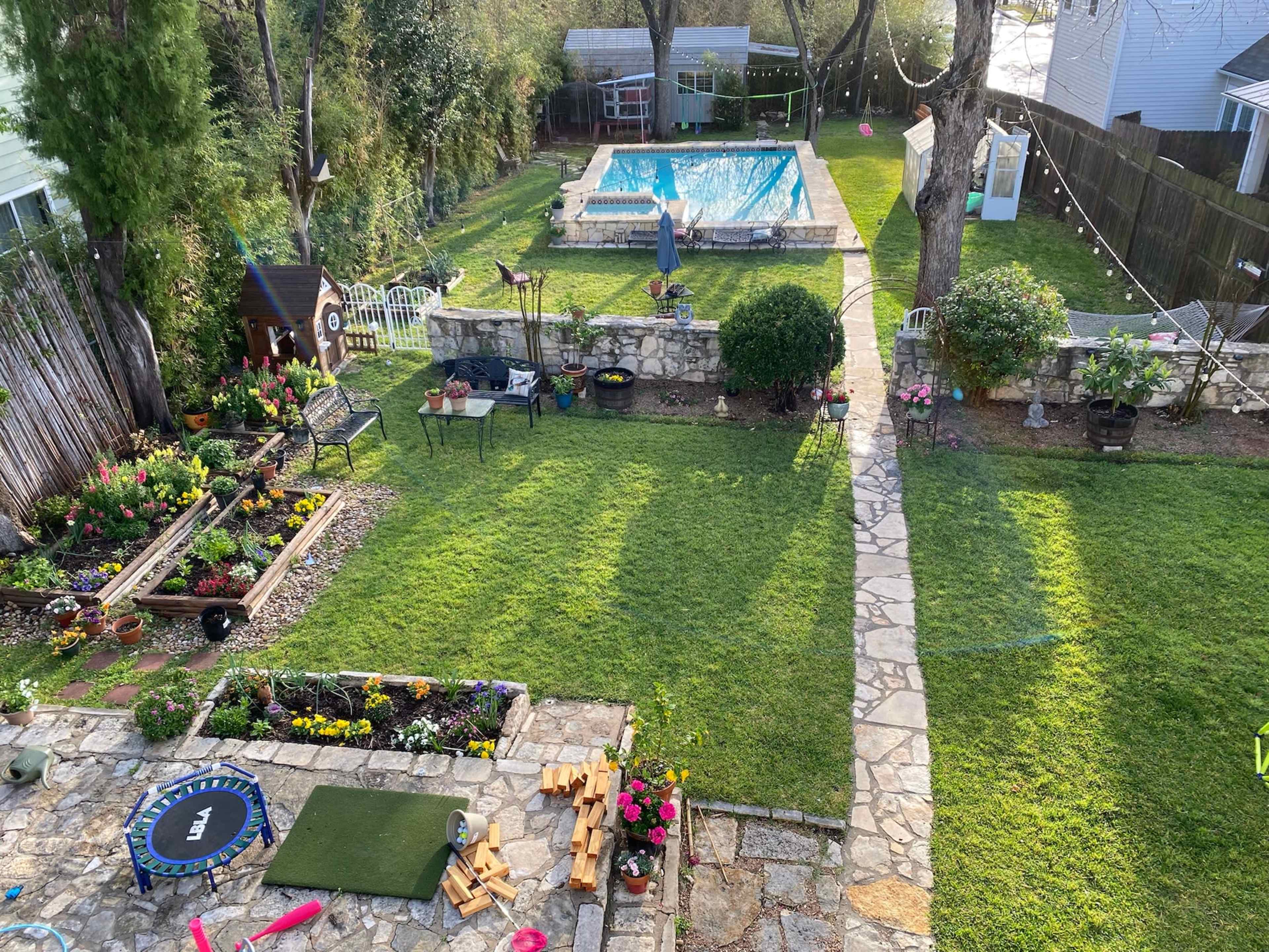 A well-maintained backyard with a swimming pool, a stone pathway, and neatly arranged flower beds.