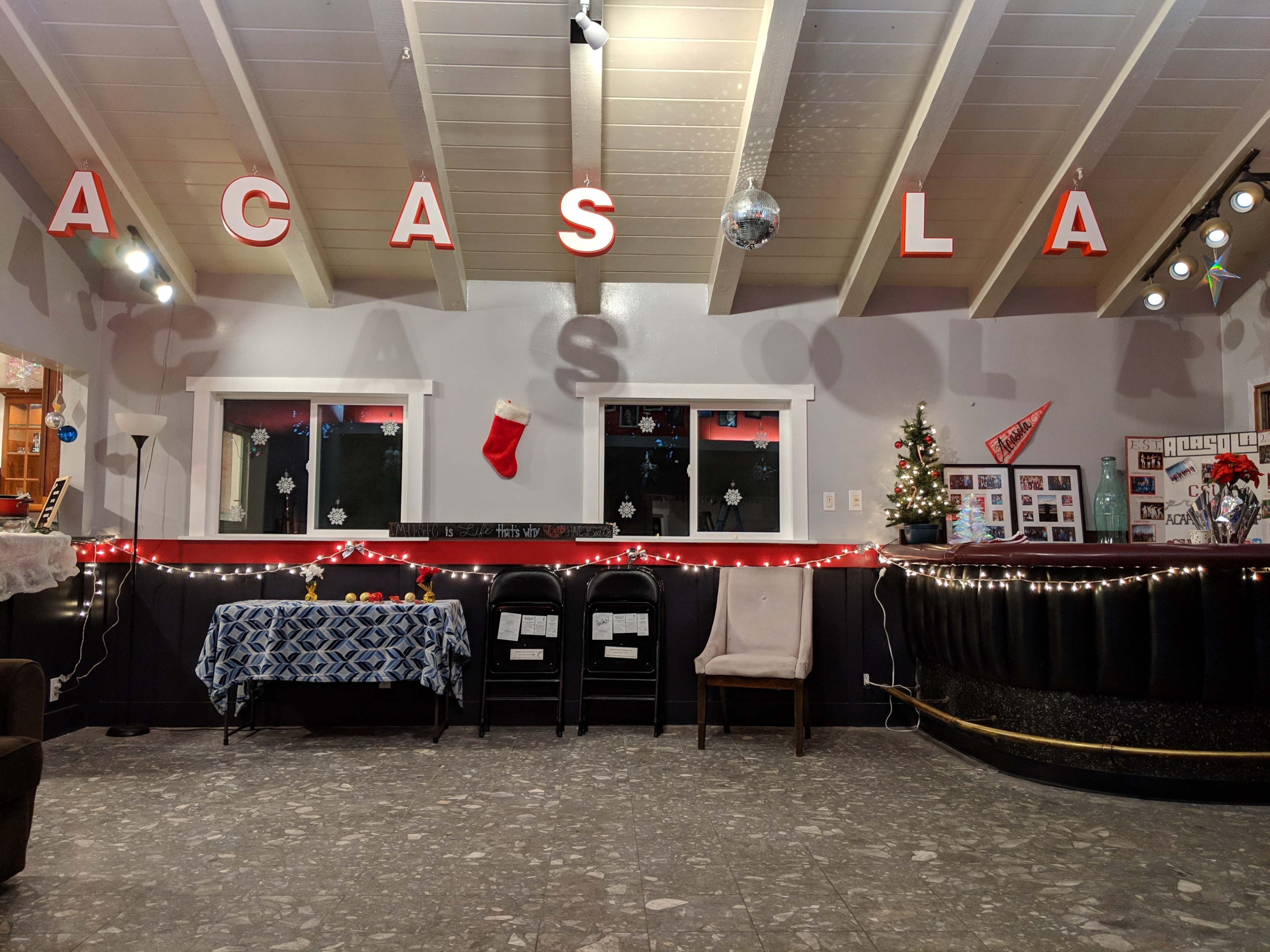 A decorated hall with a string of lights, a small Christmas tree, and a festive stocking hanging on the wall.