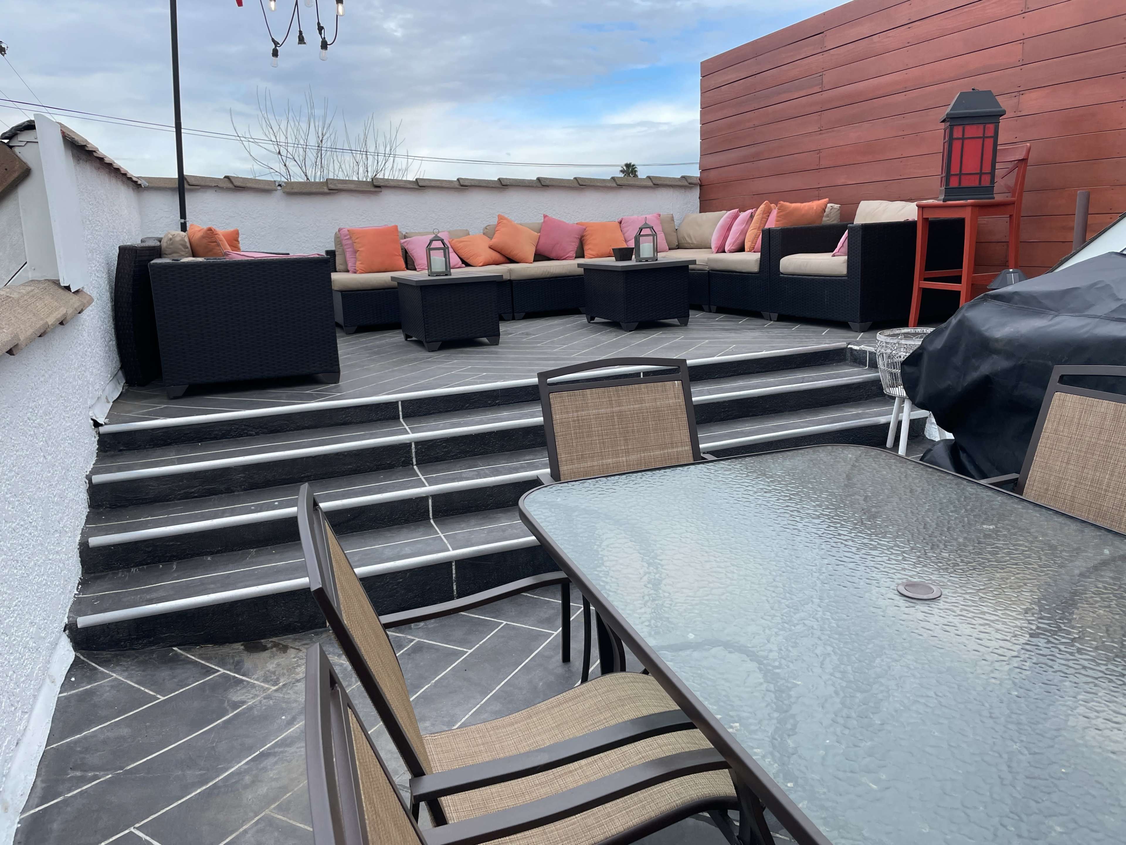 A stylish outdoor seating area features a sectional sofa with colorful cushions, a coffee table, and a dining set on a raised patio.