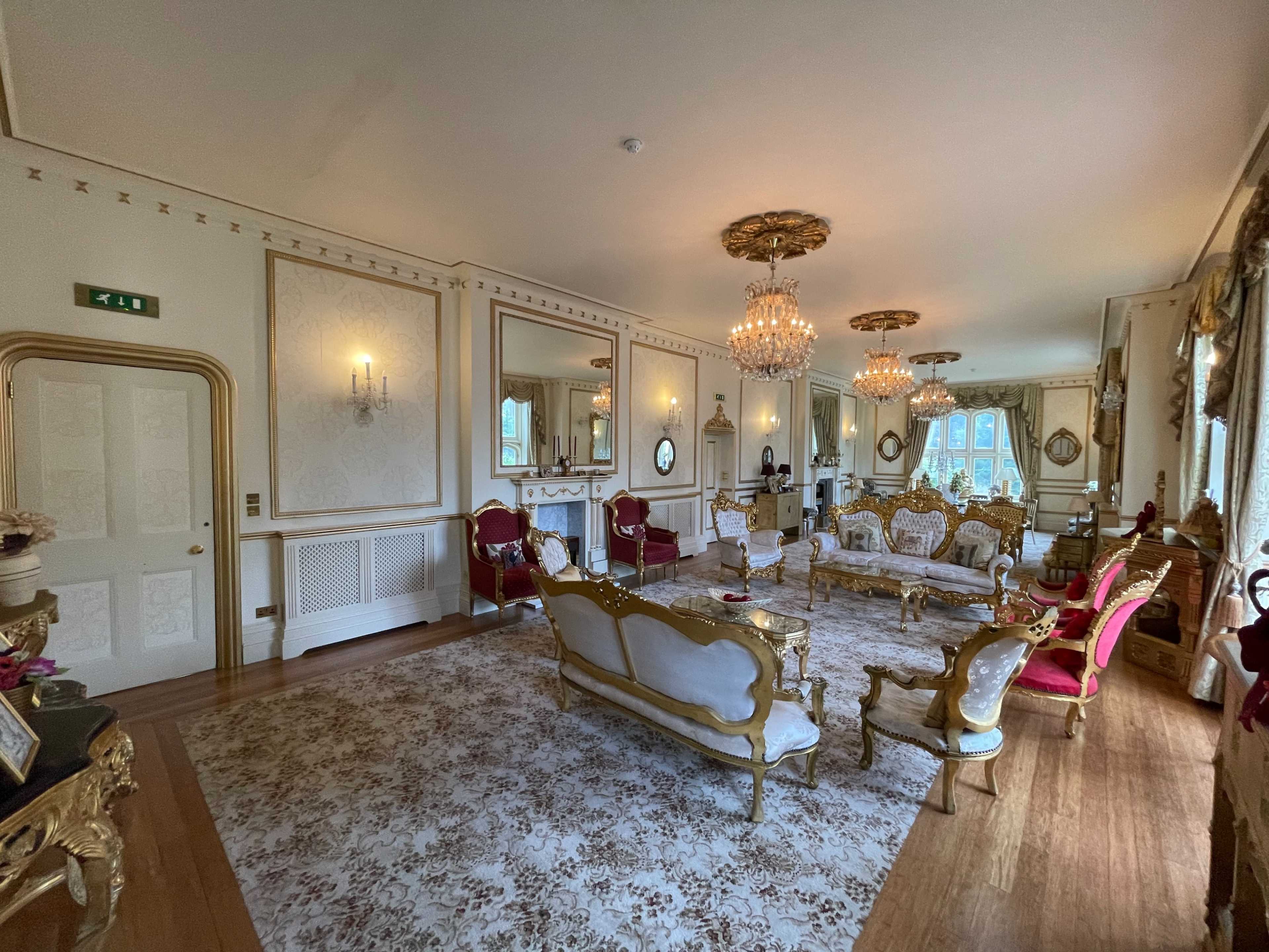 The image shows an elegantly furnished living room featuring ornate furniture, chandelier lighting, and decorative mirrors.