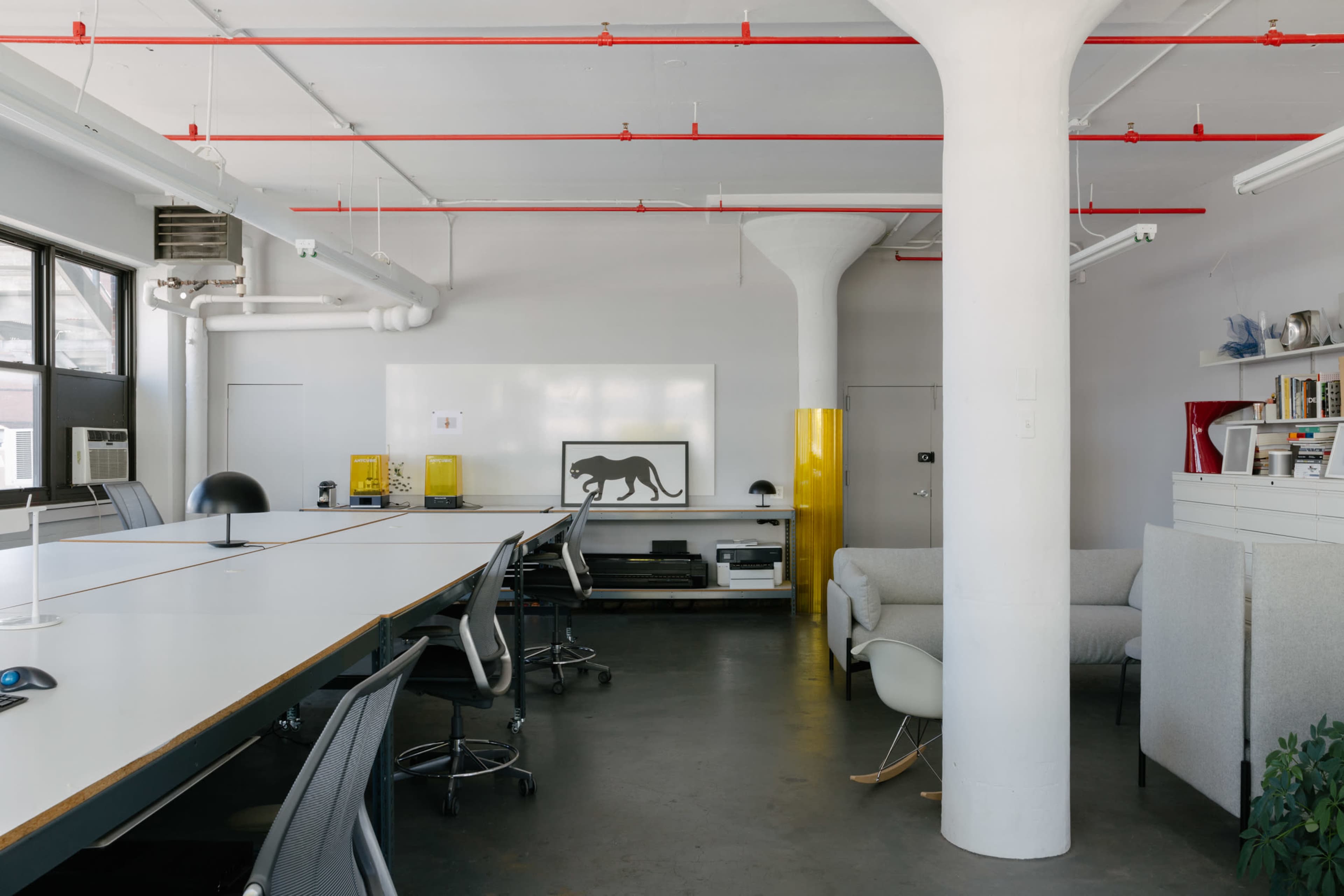 A modern office space with a large white table, ergonomic chairs, and a minimalist design featuring a black panther artwork on the wall.
